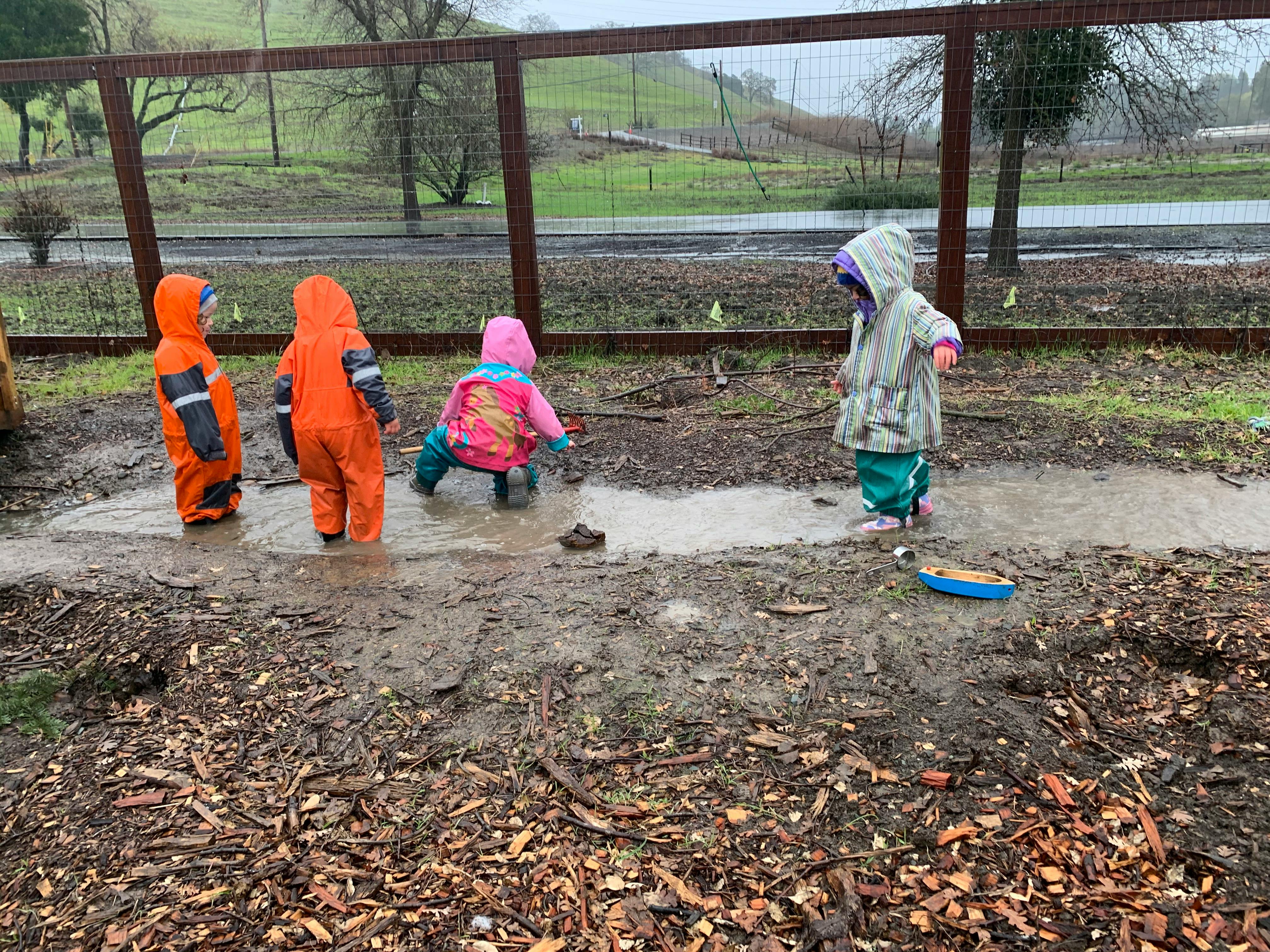 Four children playing in a muddy puddle outdoors