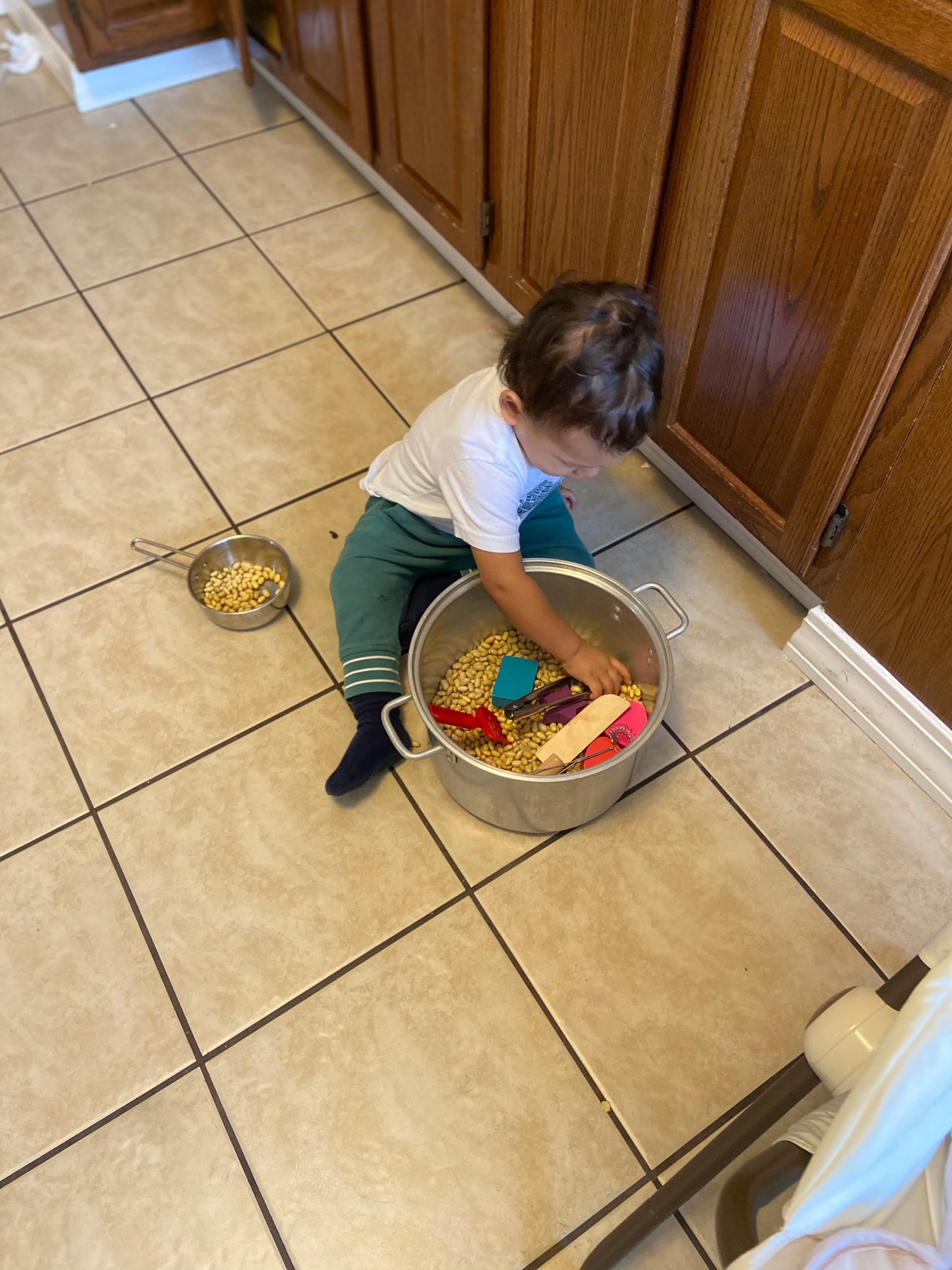 Child playing with items in a large pot on a kitchen floor