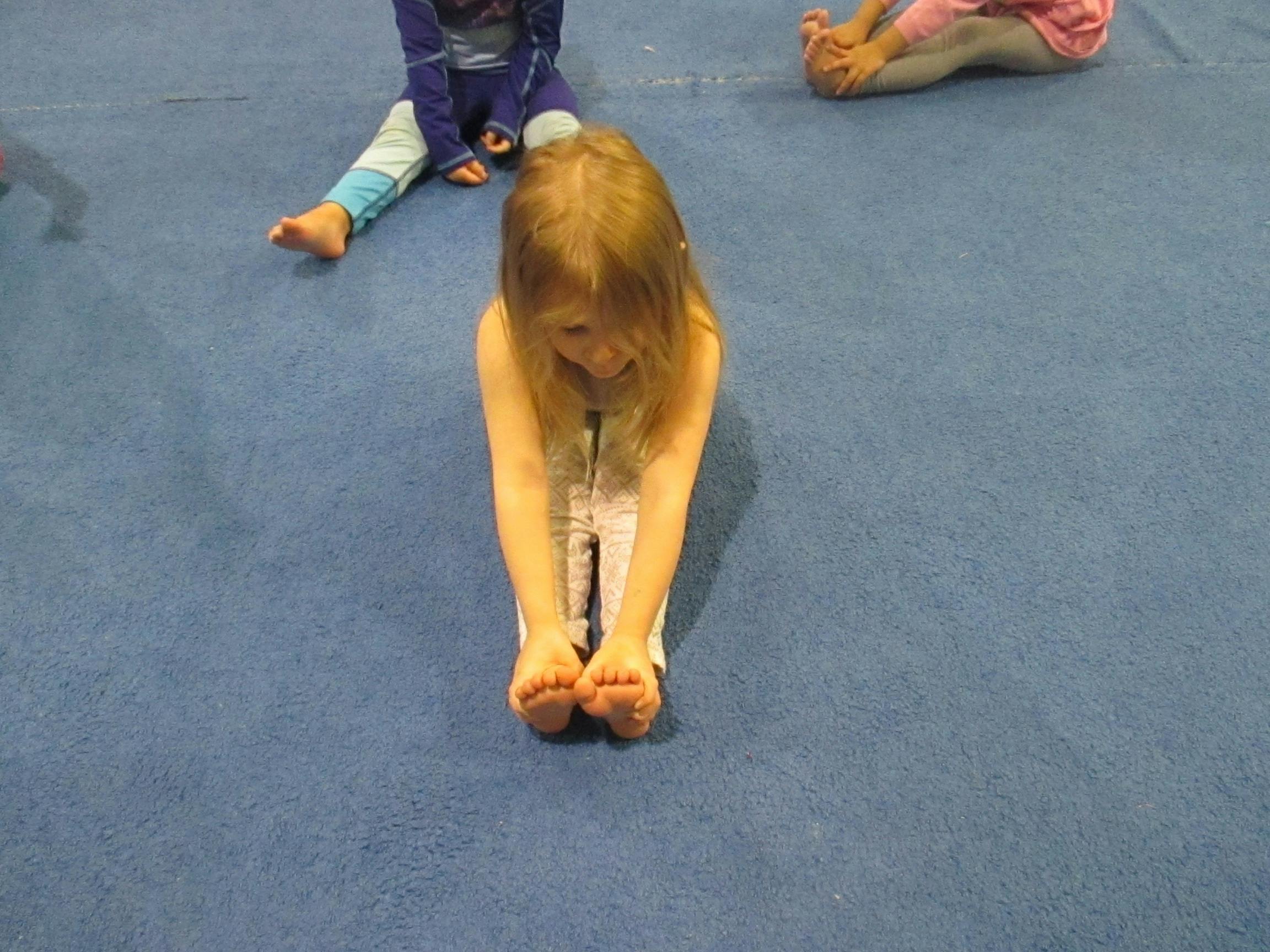 Child sitting on blue mat, stretching forward and touching feet