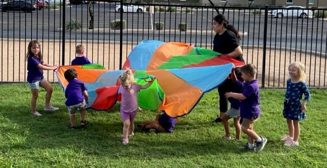Adult and children playing with a colorful parachute on grass