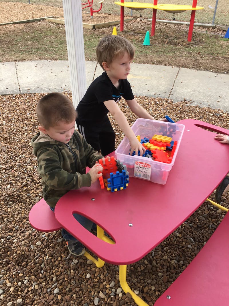 Two children playing with colorful building blocks at a red table outdoors