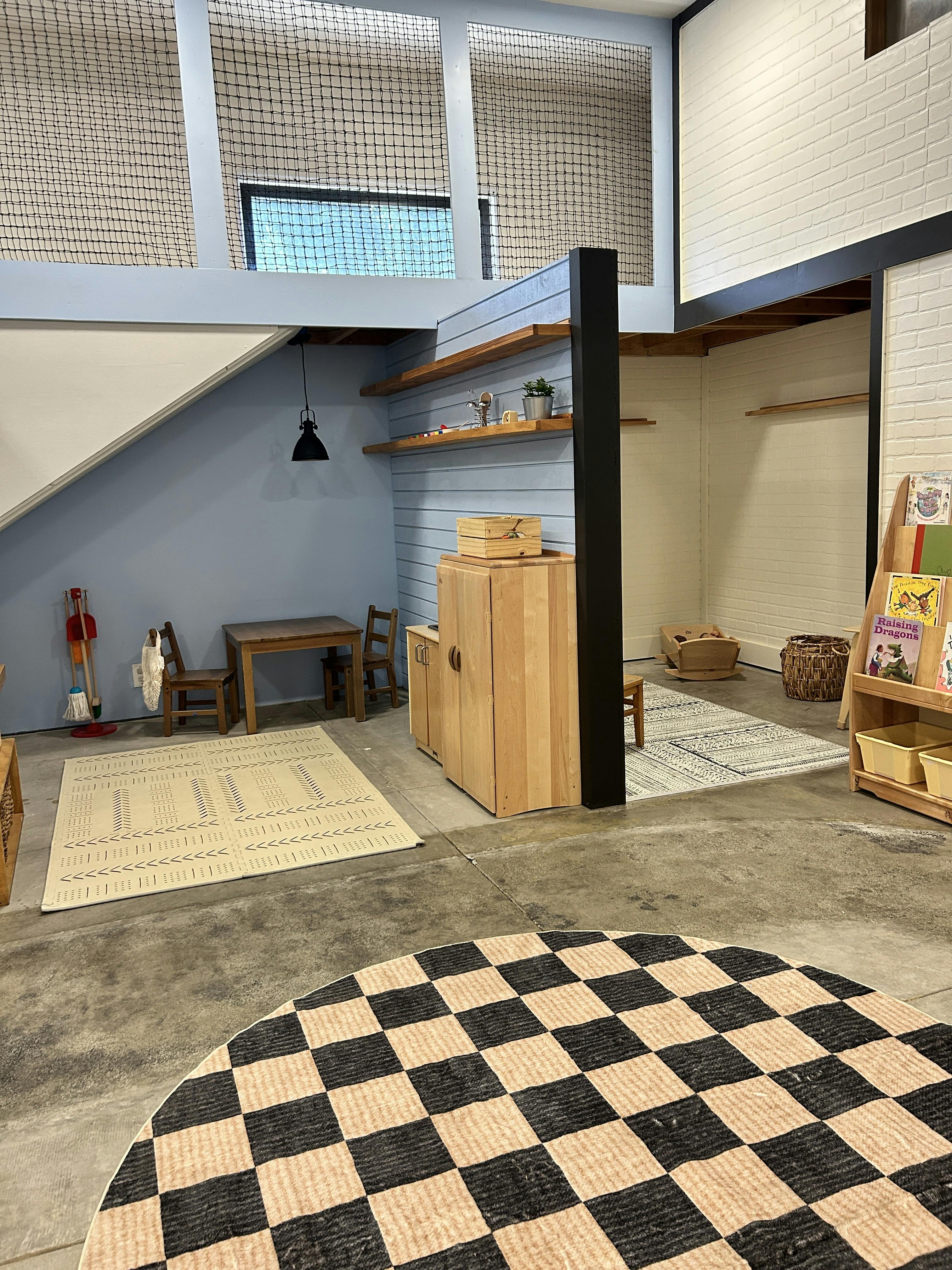 Children's play area with small wooden furniture, rugs, and shelves