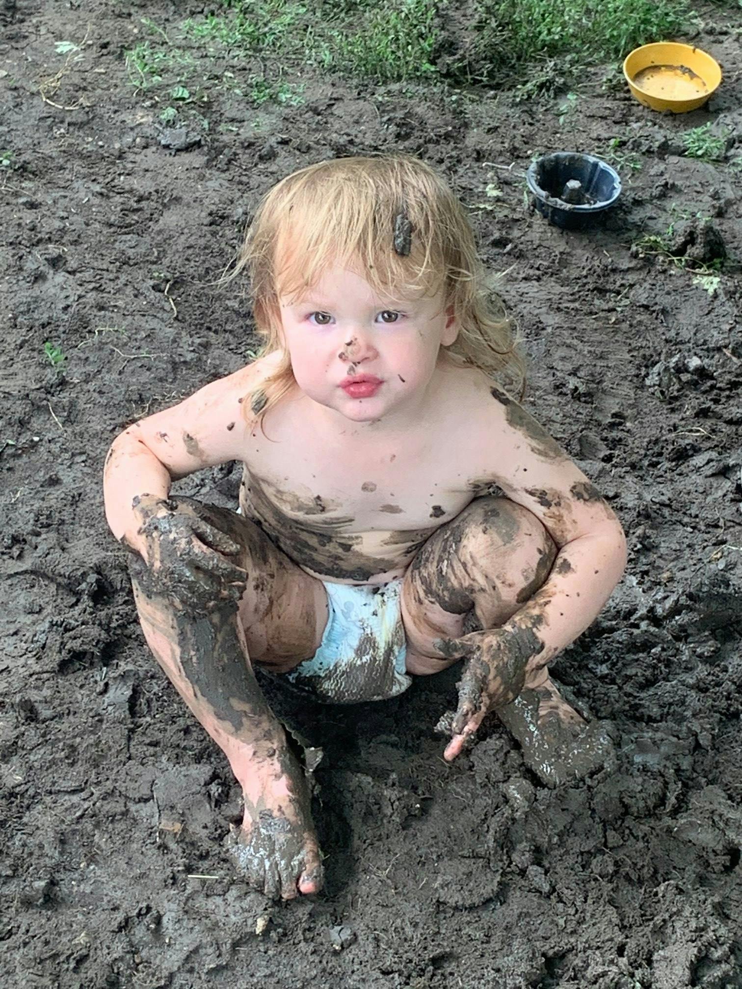 Child covered in mud sitting on the ground