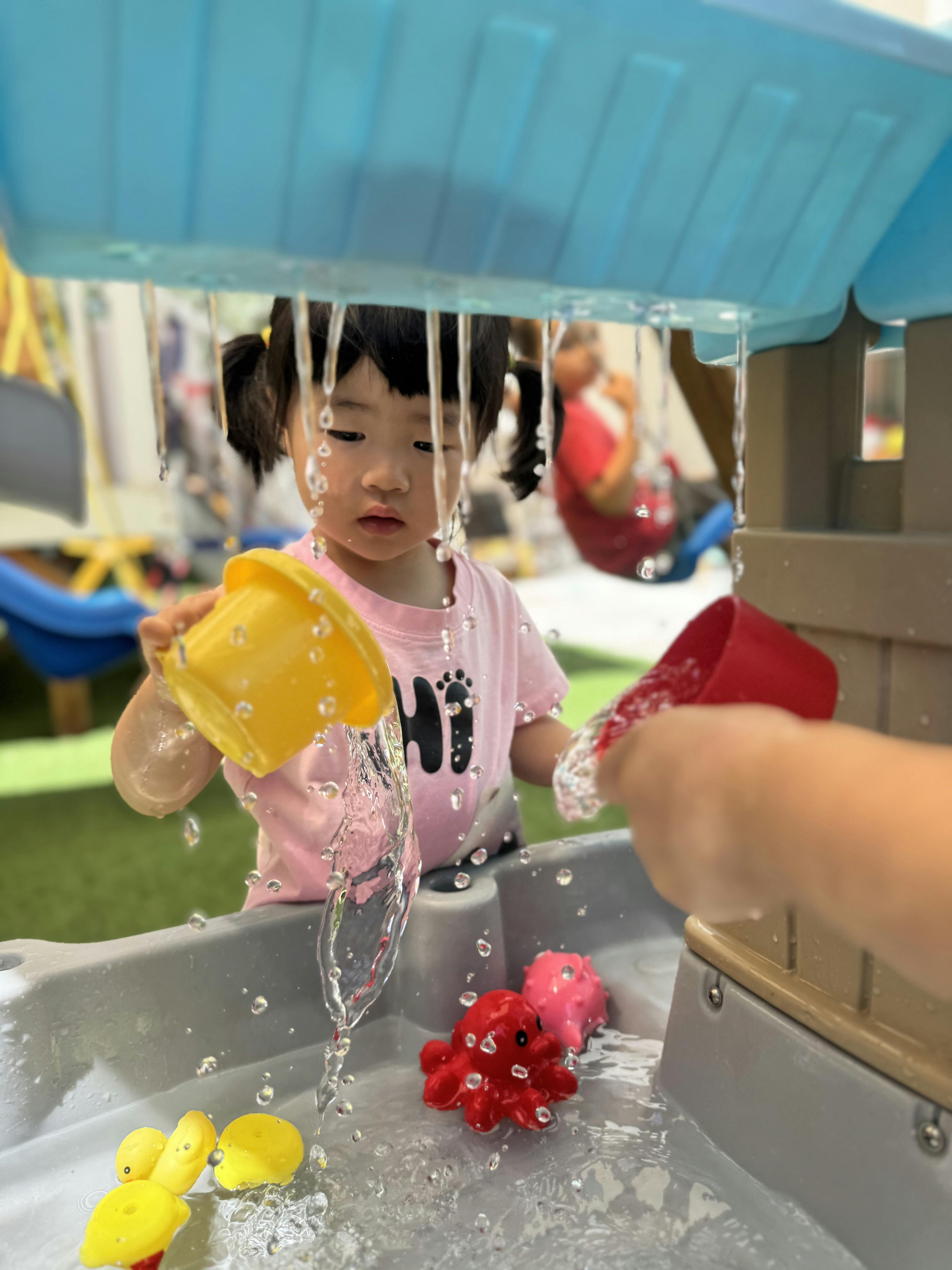 Child pouring water from a plastic cup at a water table