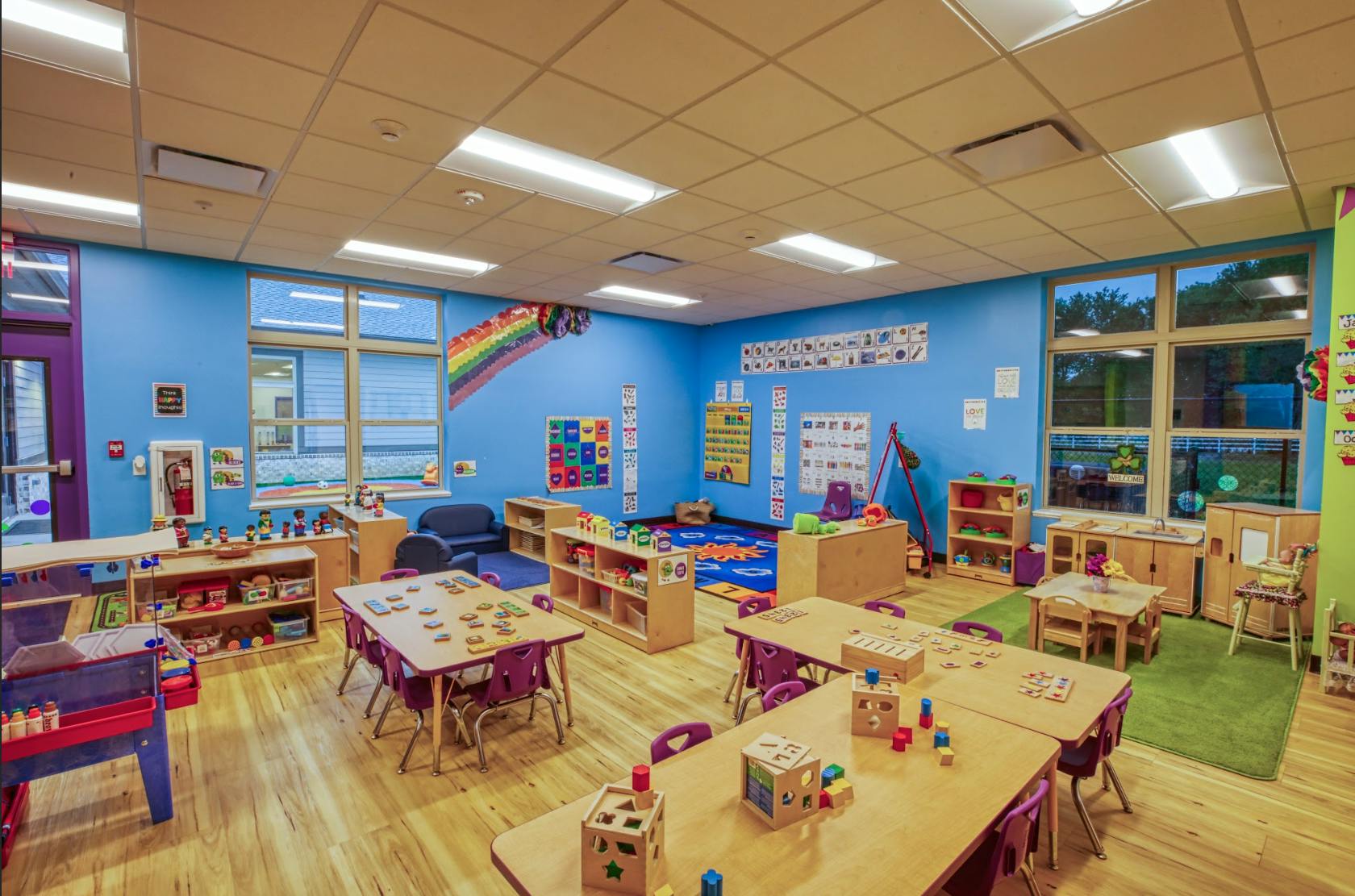 Classroom with small tables and chairs, shelves with toys, and blue walls