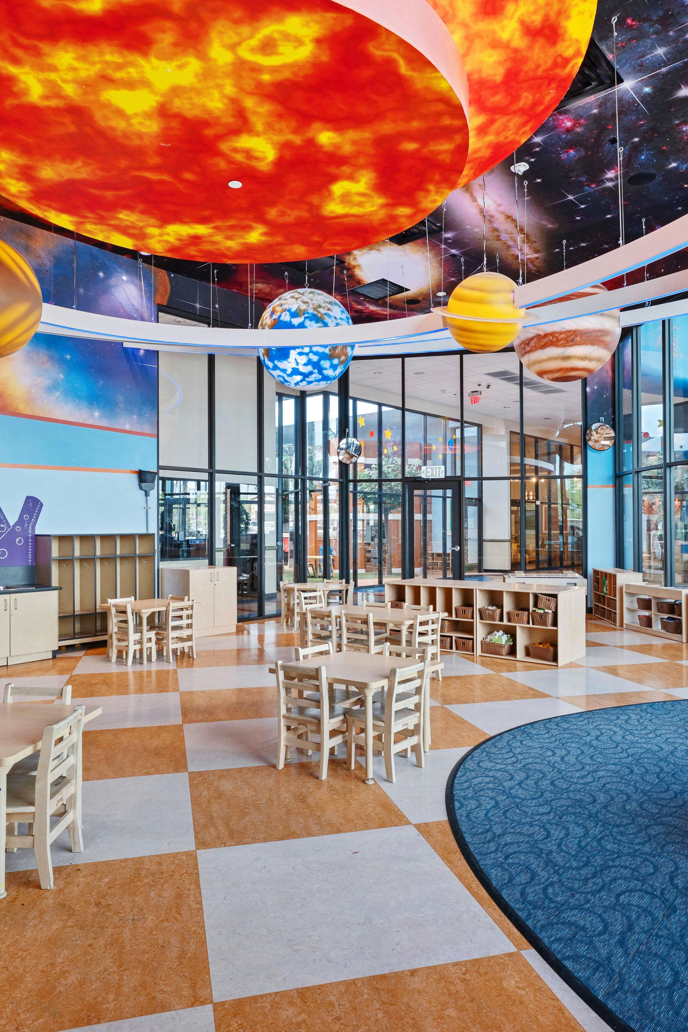 Classroom decorated with planets and solar system ceiling, child-sized tables