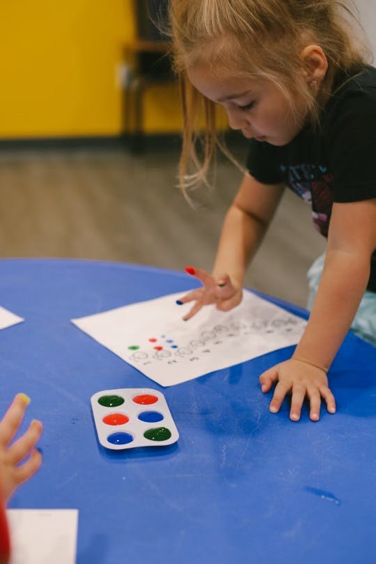 Child finger painting on paper with a paint palette on a blue table