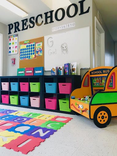 Preschool classroom with a whiteboard, storage bins, and alphabet mat