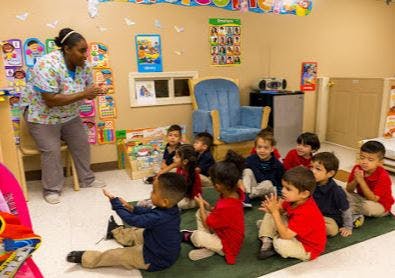 Adult speaking to a group of children sitting on the floor in a classroom