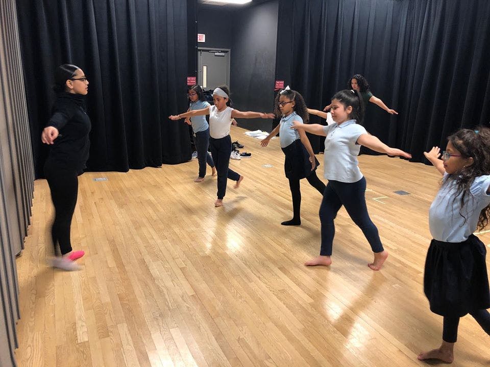 Adult and children in a dance studio with arms extended