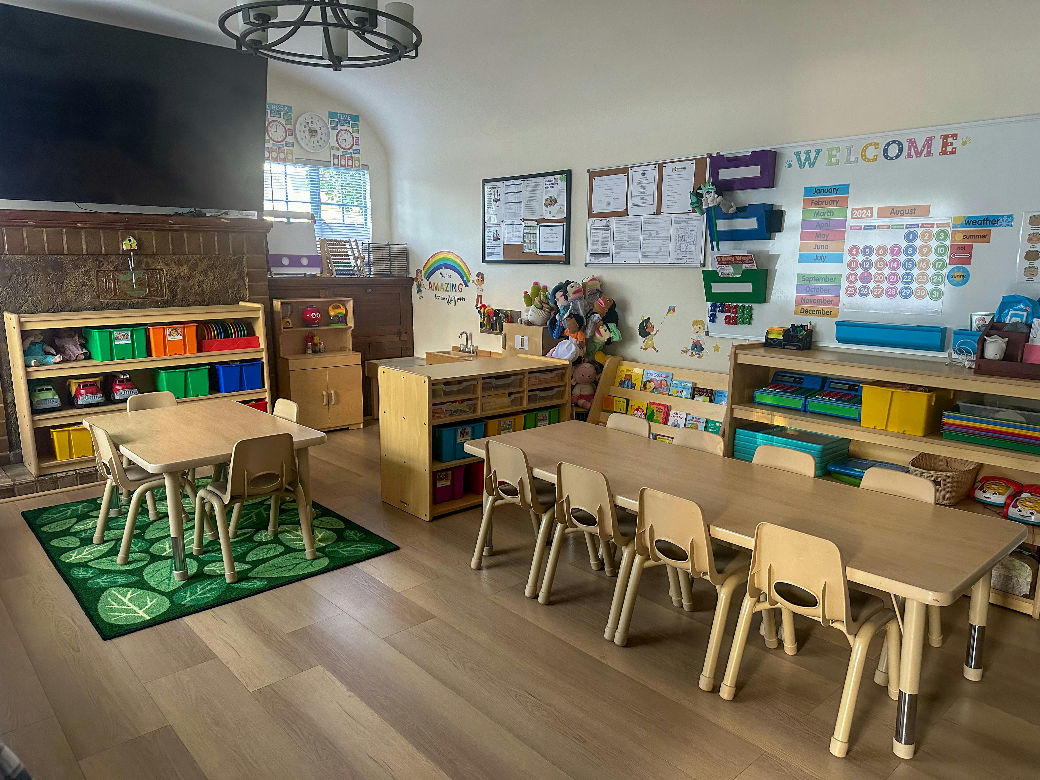 Classroom with small tables and chairs, shelves with colorful bins