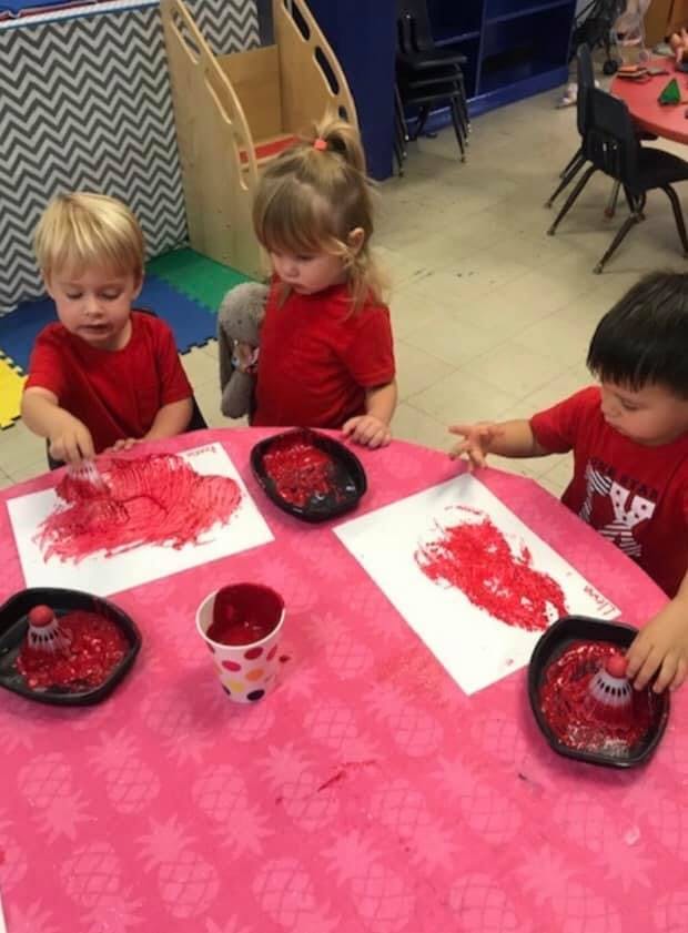 Three children painting with red paint at a table