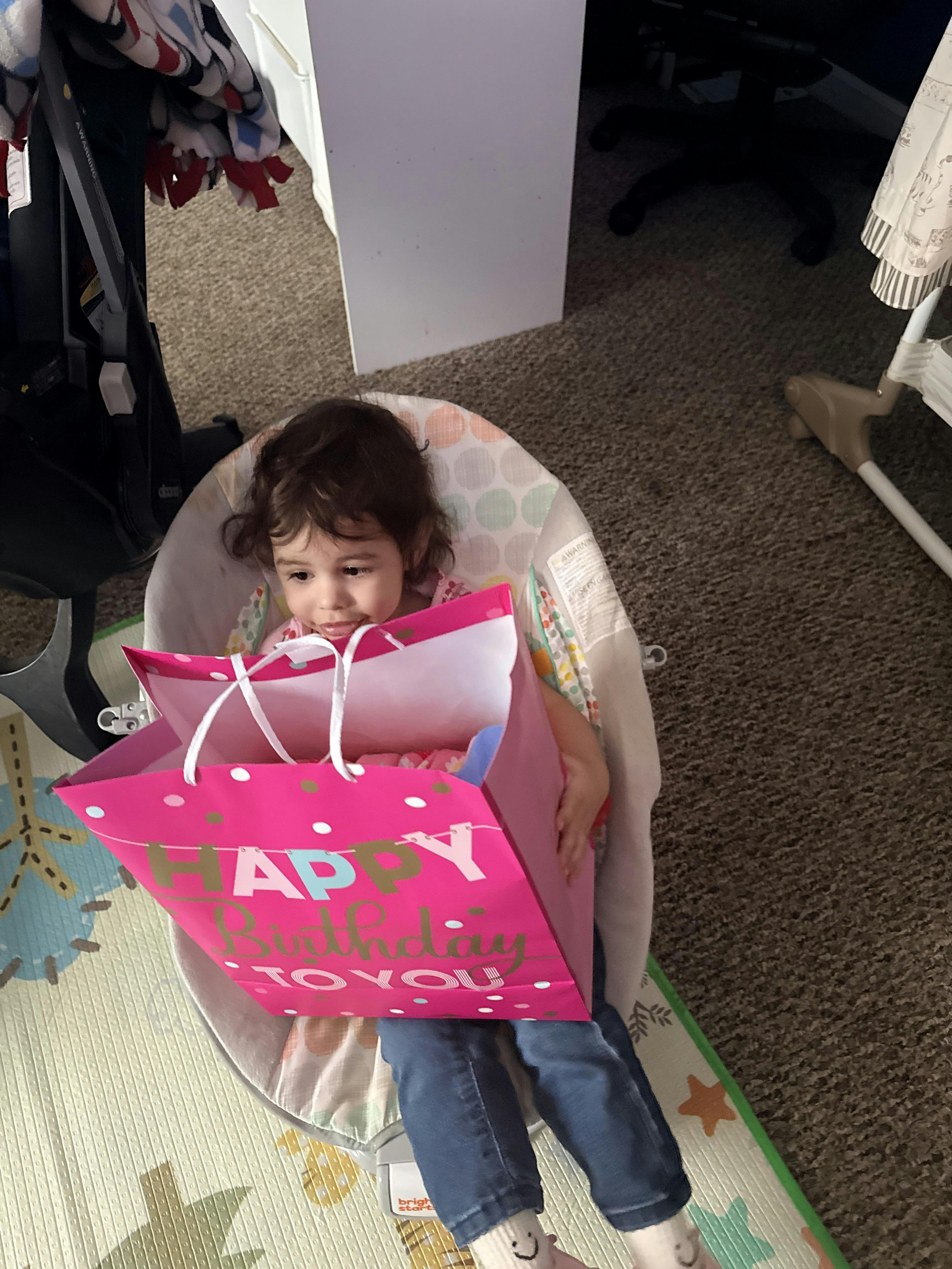 Child in a bouncer holding a pink Happy Birthday gift bag