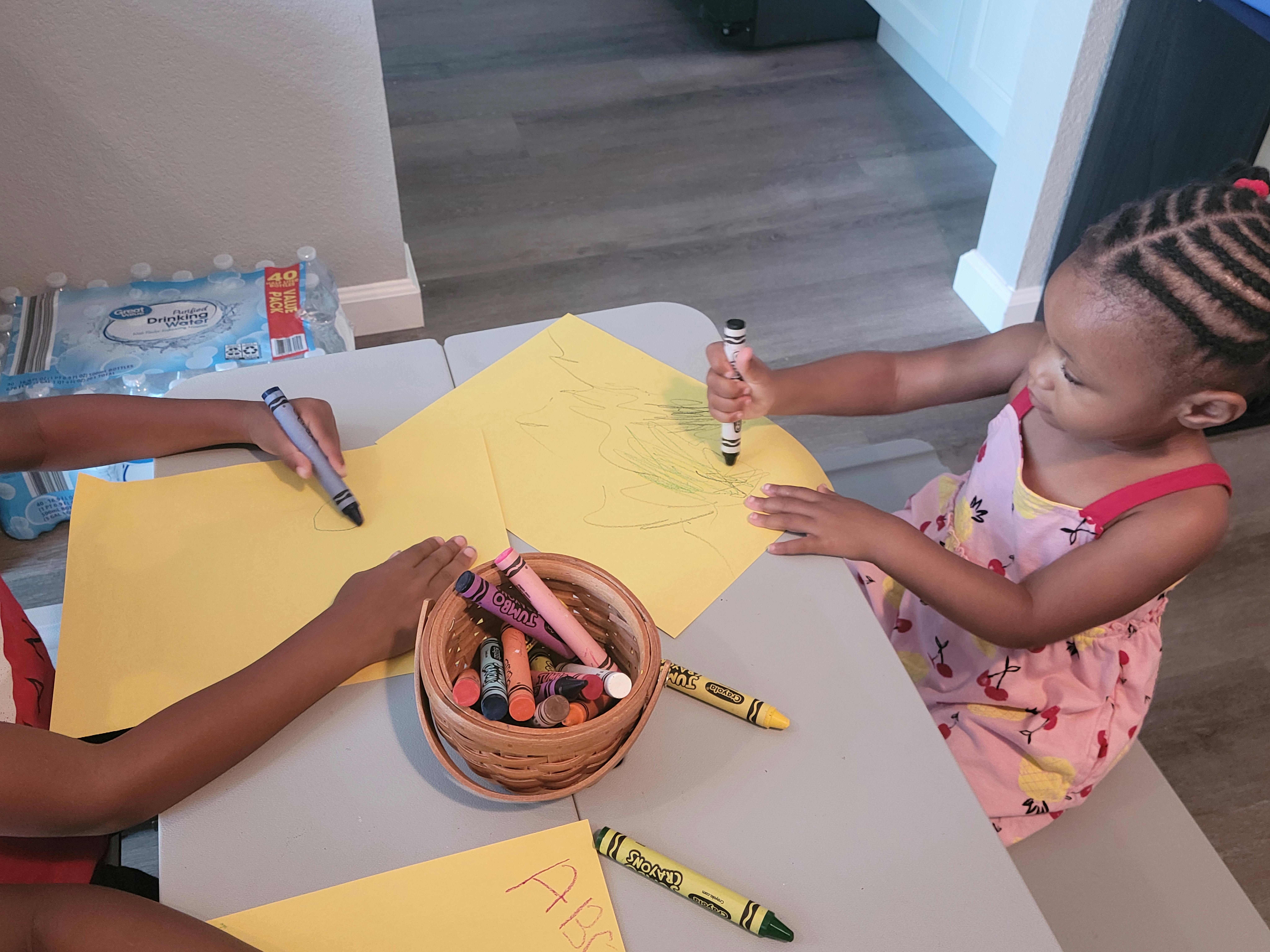 Two children drawing on yellow paper with markers