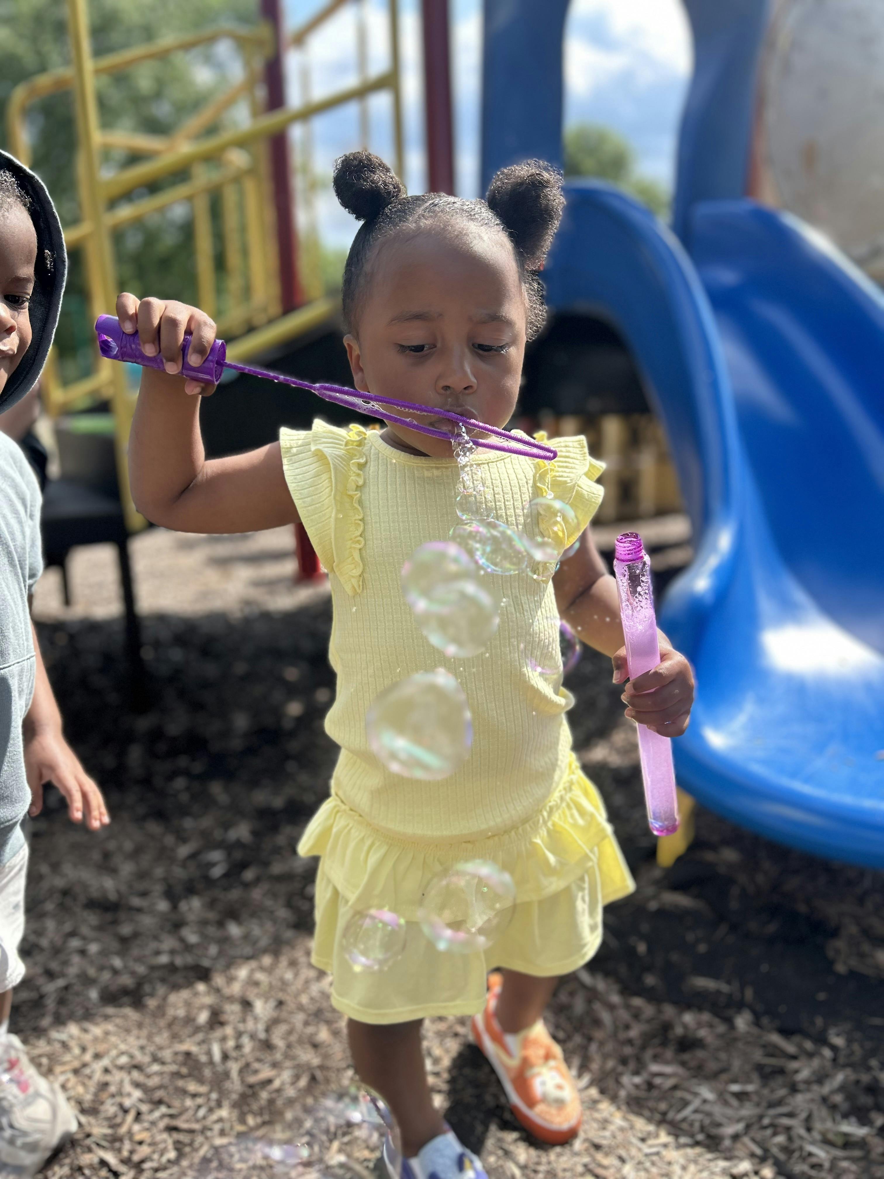 Child blowing bubbles with a bubble wand at a playground
