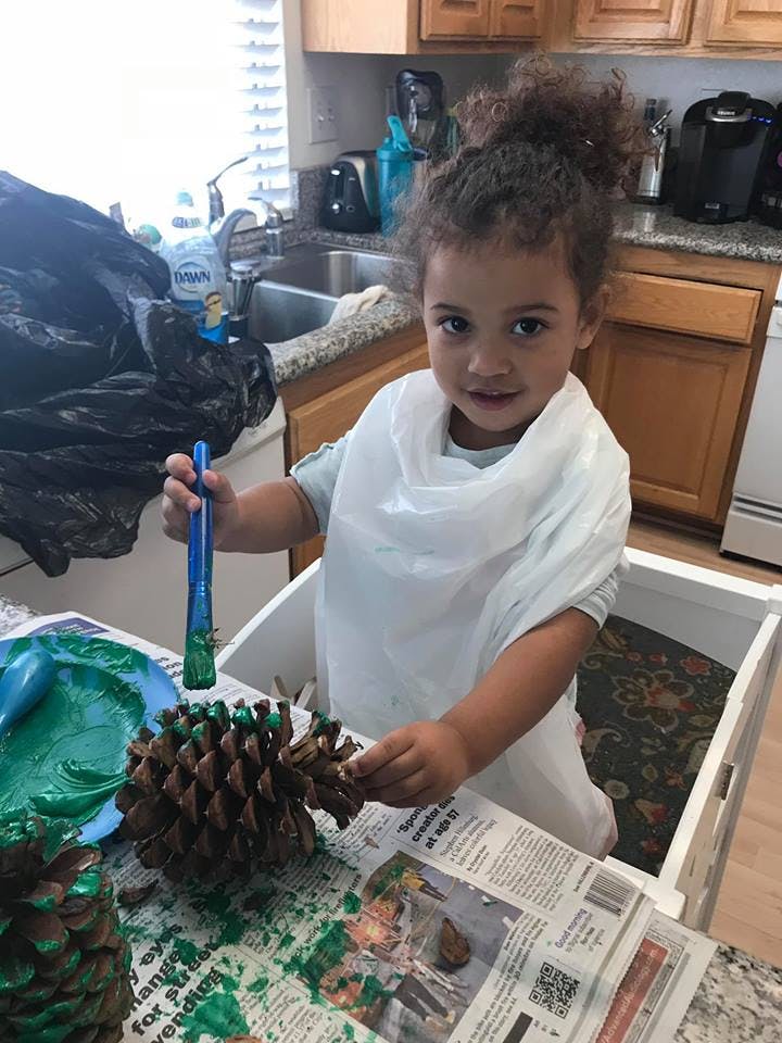 Child painting a pinecone green with a paintbrush
