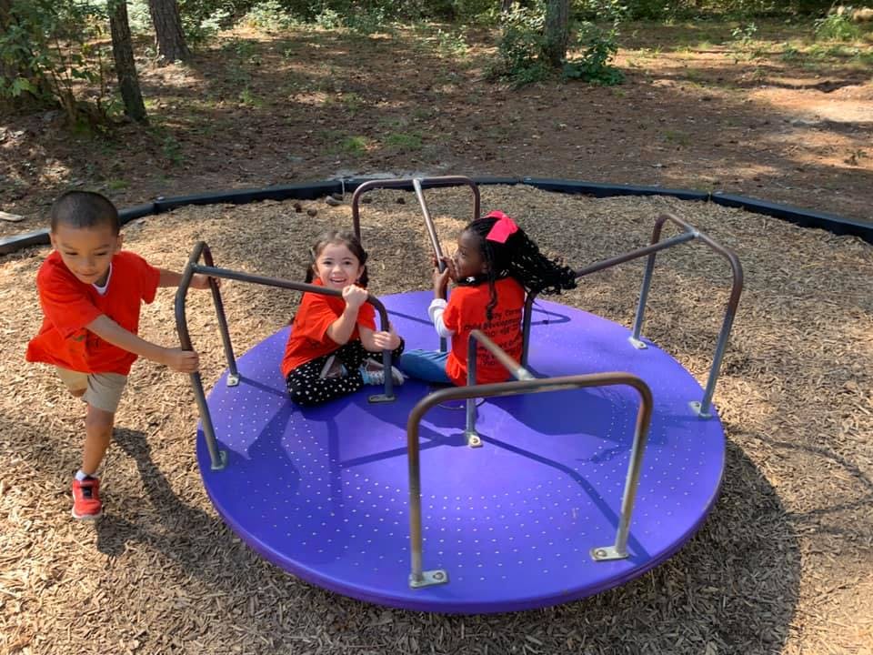 Three children playing on a merry-go-round at a playground