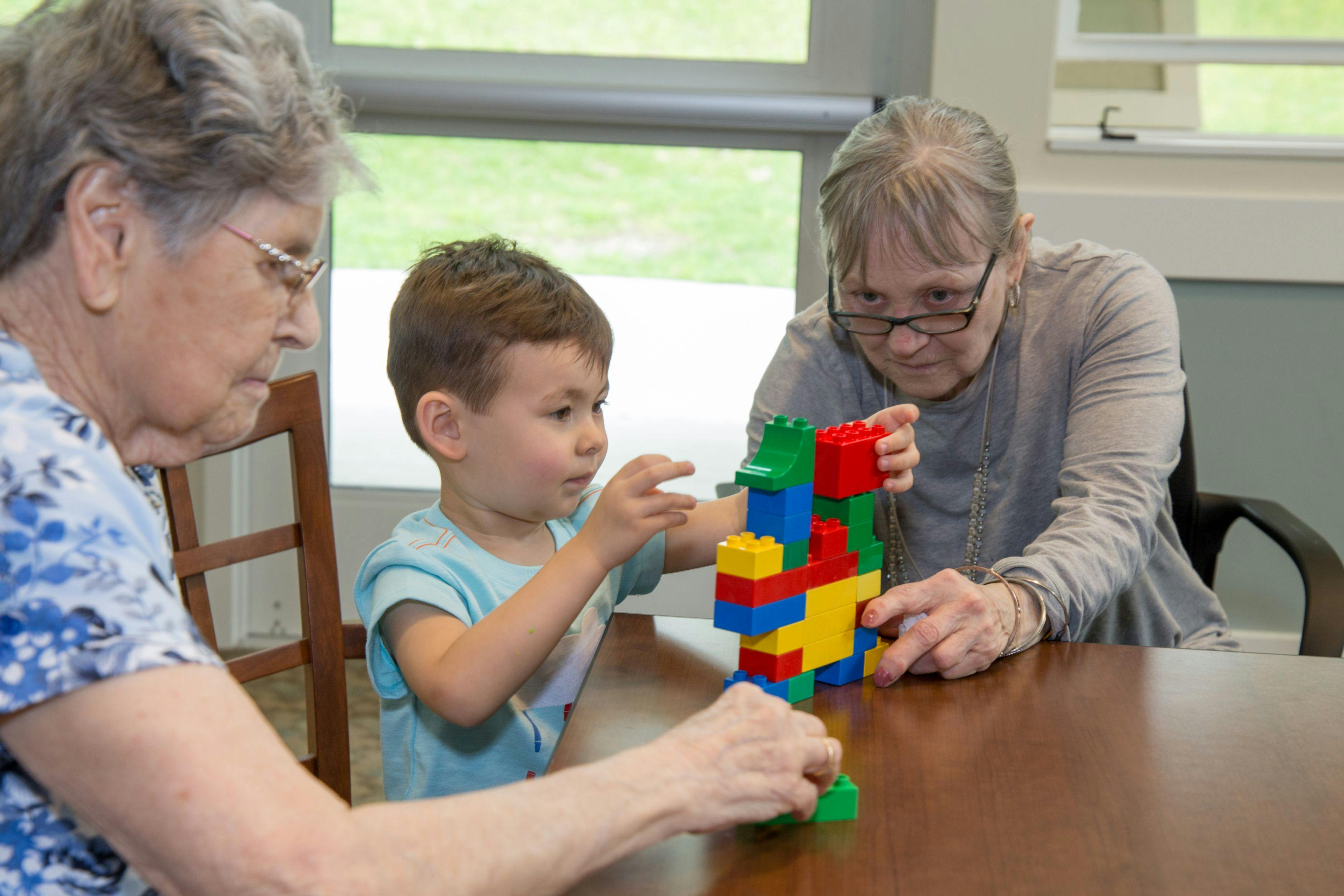 Two people and a child playing with colorful building blocks at a table