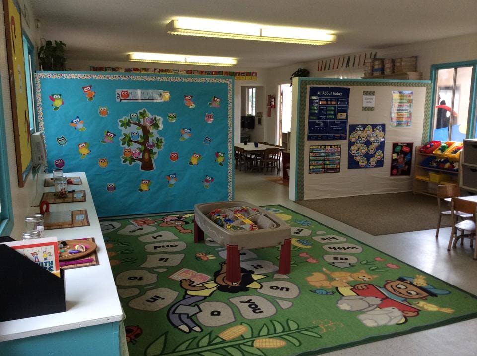 Classroom with a green rug, play table, and blue partition with decorations