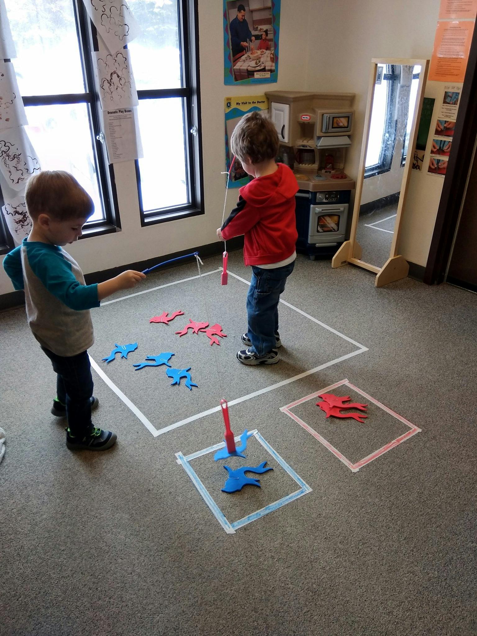 Two children playing with magnetic fishing rods and fish cutouts in a classroom