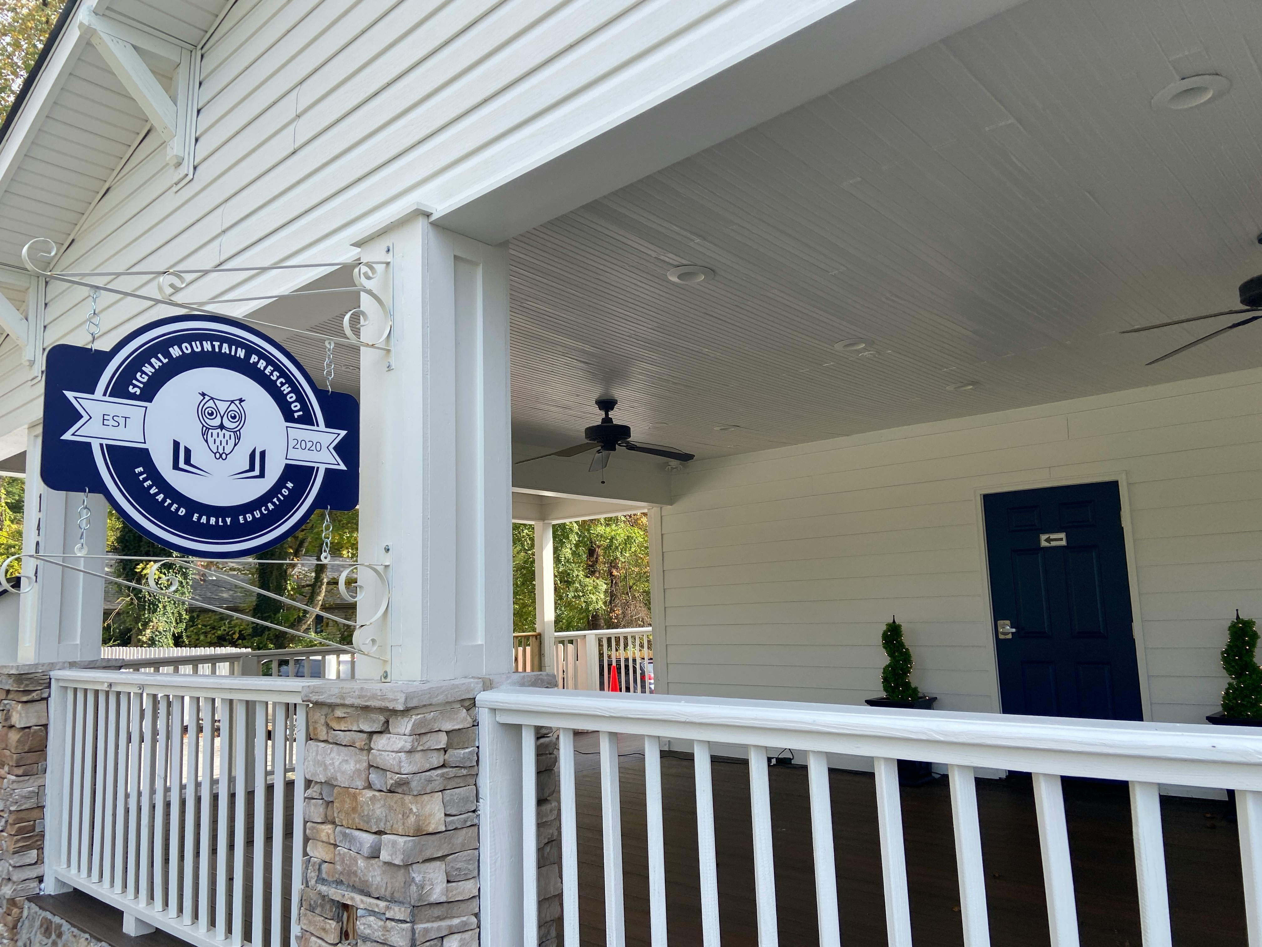 Blue and white sign for "Signal Mountain Preschool" hanging on a porch