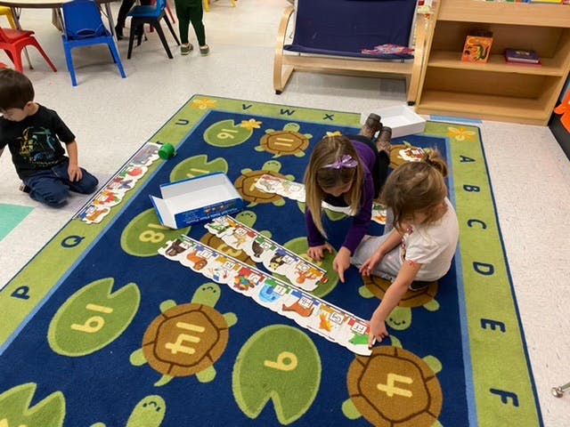 Children playing with puzzle strips on a rug in a classroom