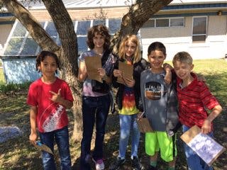 Five children standing outdoors with clipboards