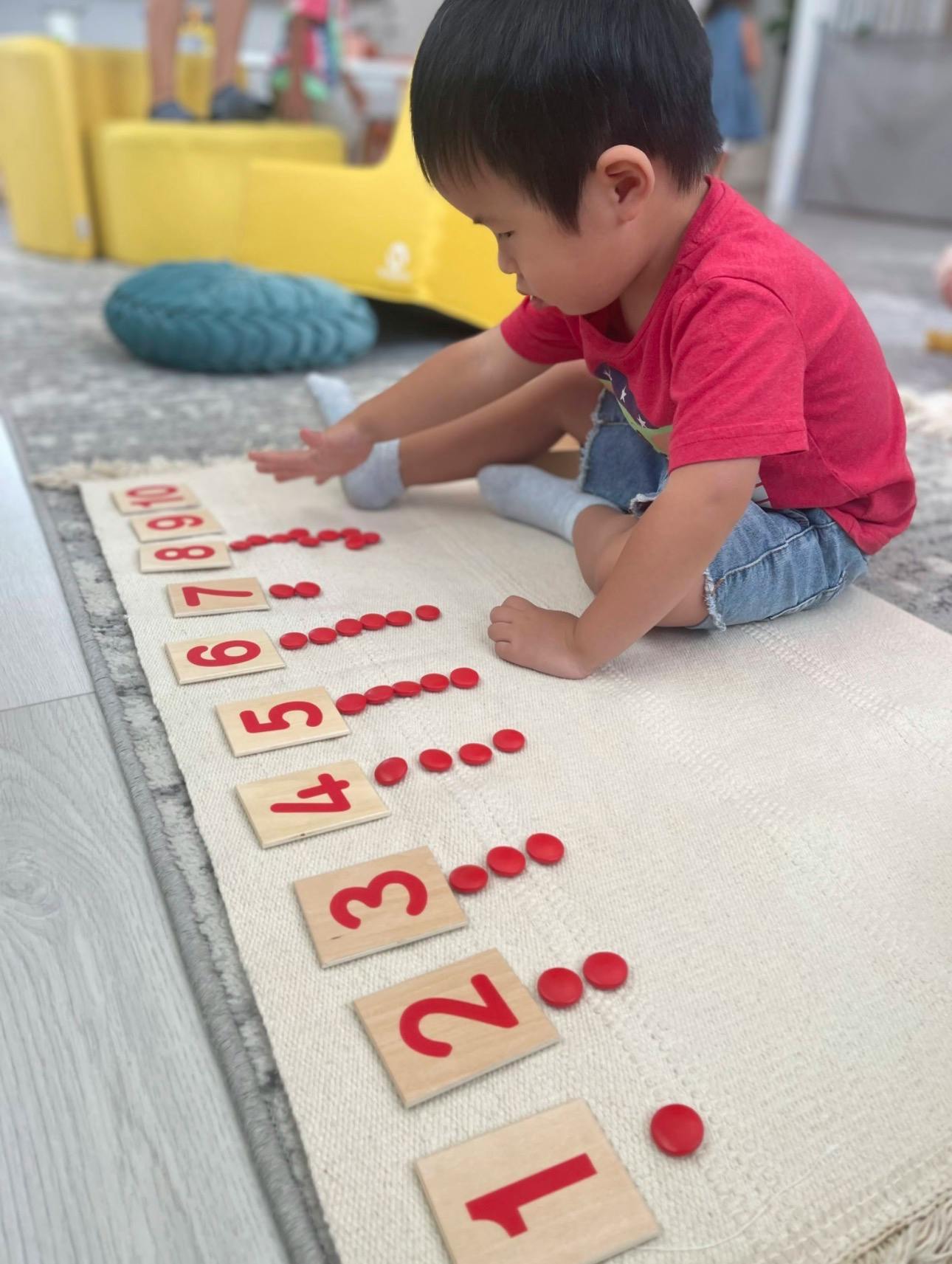 Child sitting on a rug playing with wooden number tiles and red counting discs