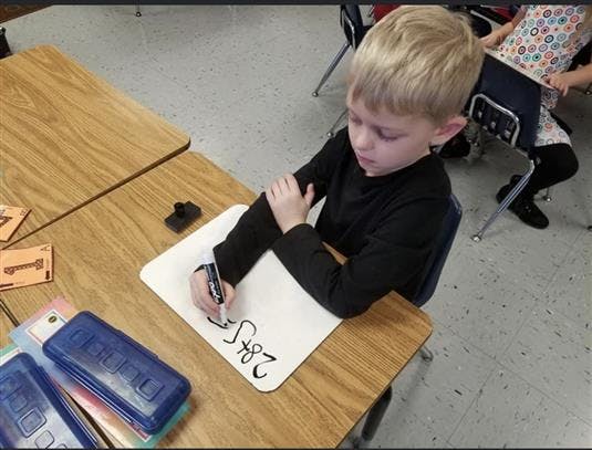 Child writing on a whiteboard at a desk in a classroom