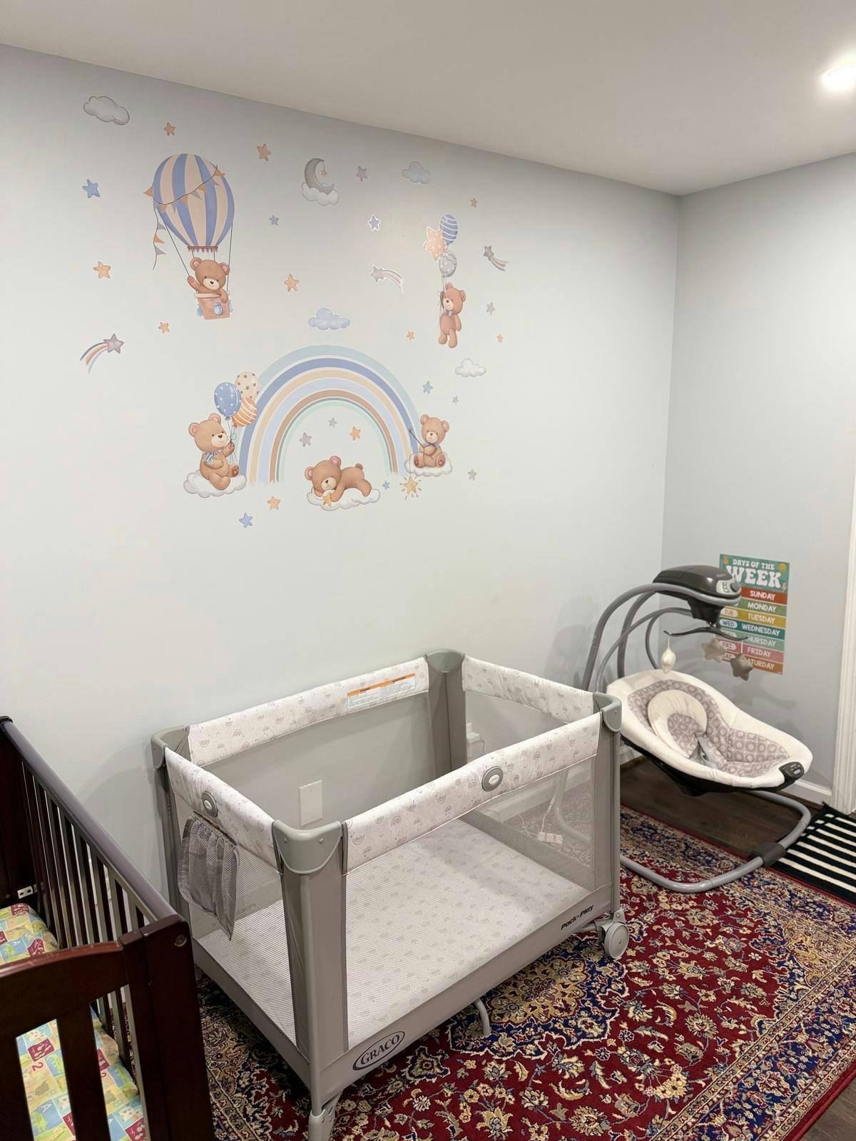 A nursery with a playard, bassinet, and wall decals of teddy bears and a rainbow