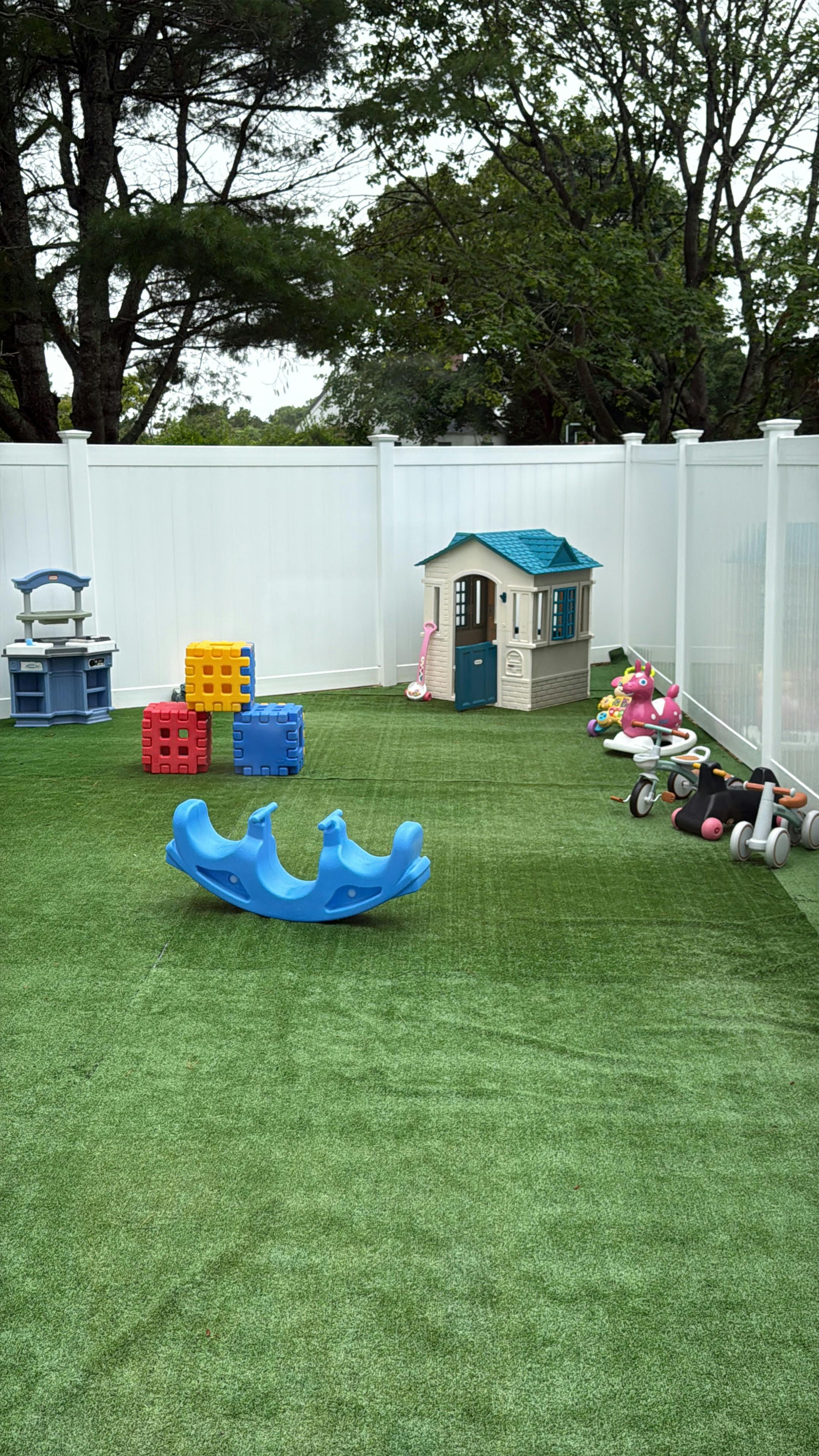 Playground equipment including a plastic playhouse and toys on artificial grass
