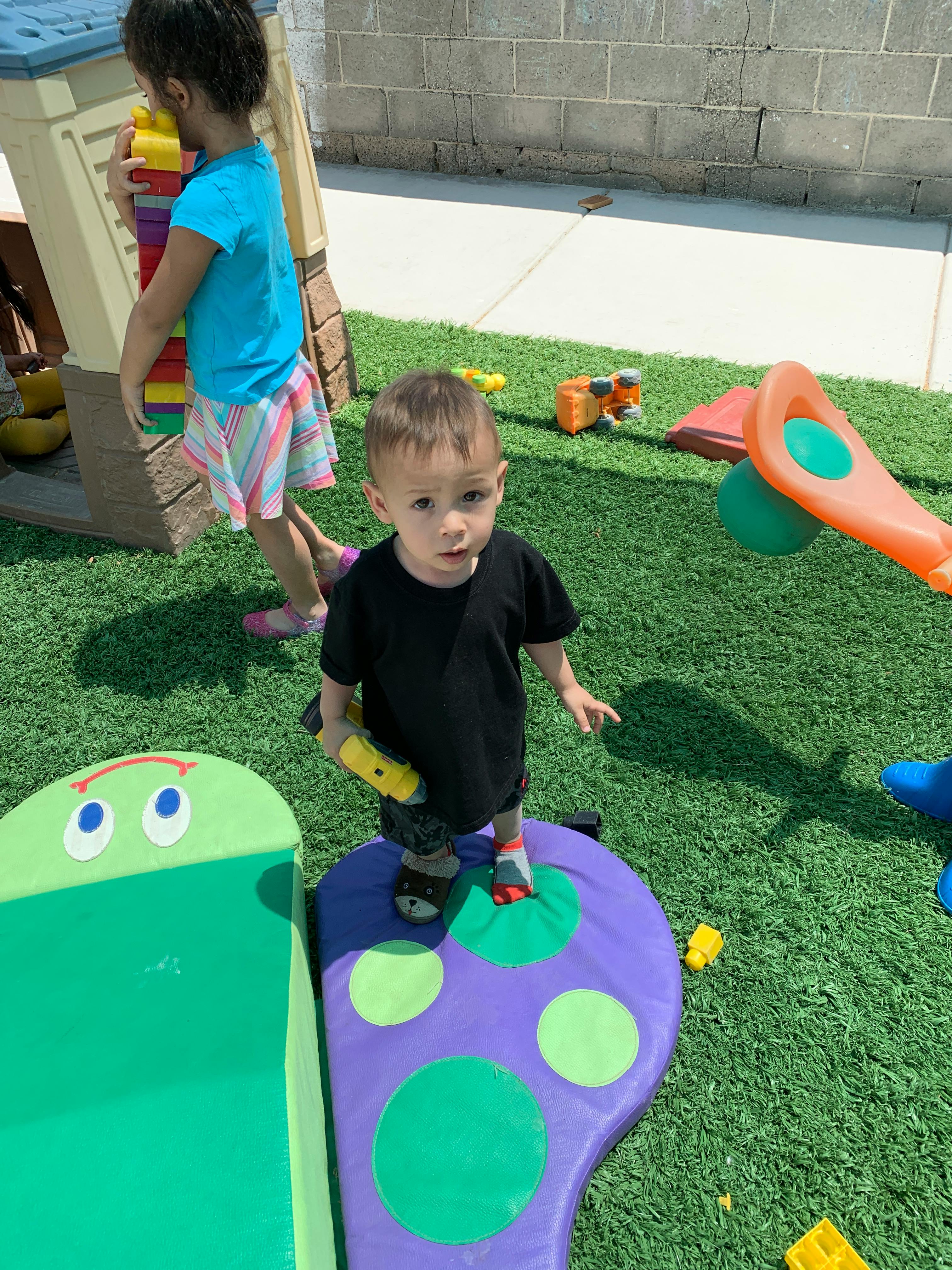 Child standing on a purple play mat with another child in the background