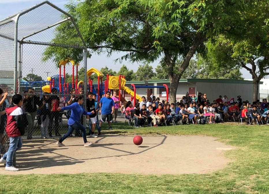 Children playing kickball on a field with a playground in the background