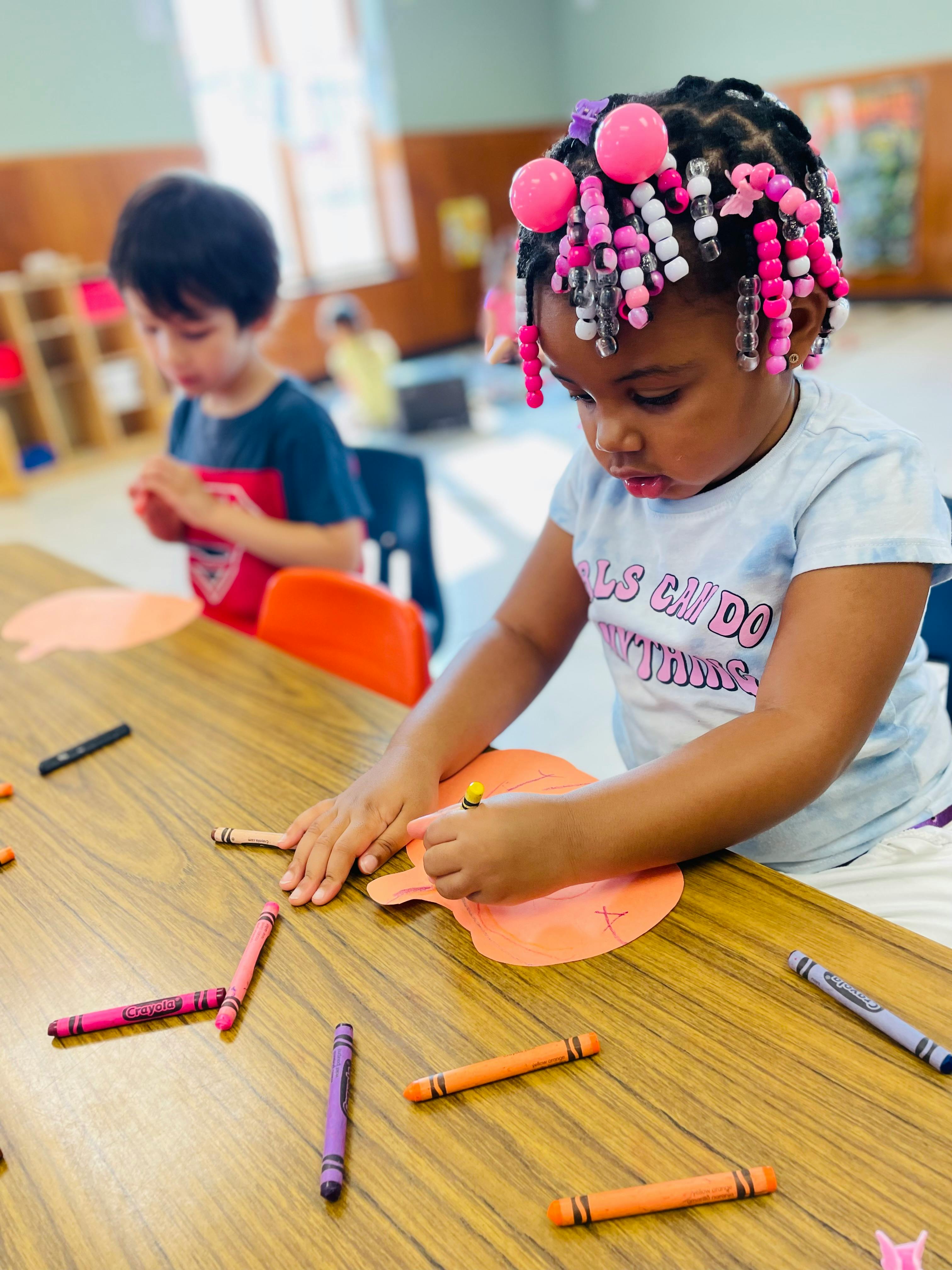 Child coloring at a table with another child in the background