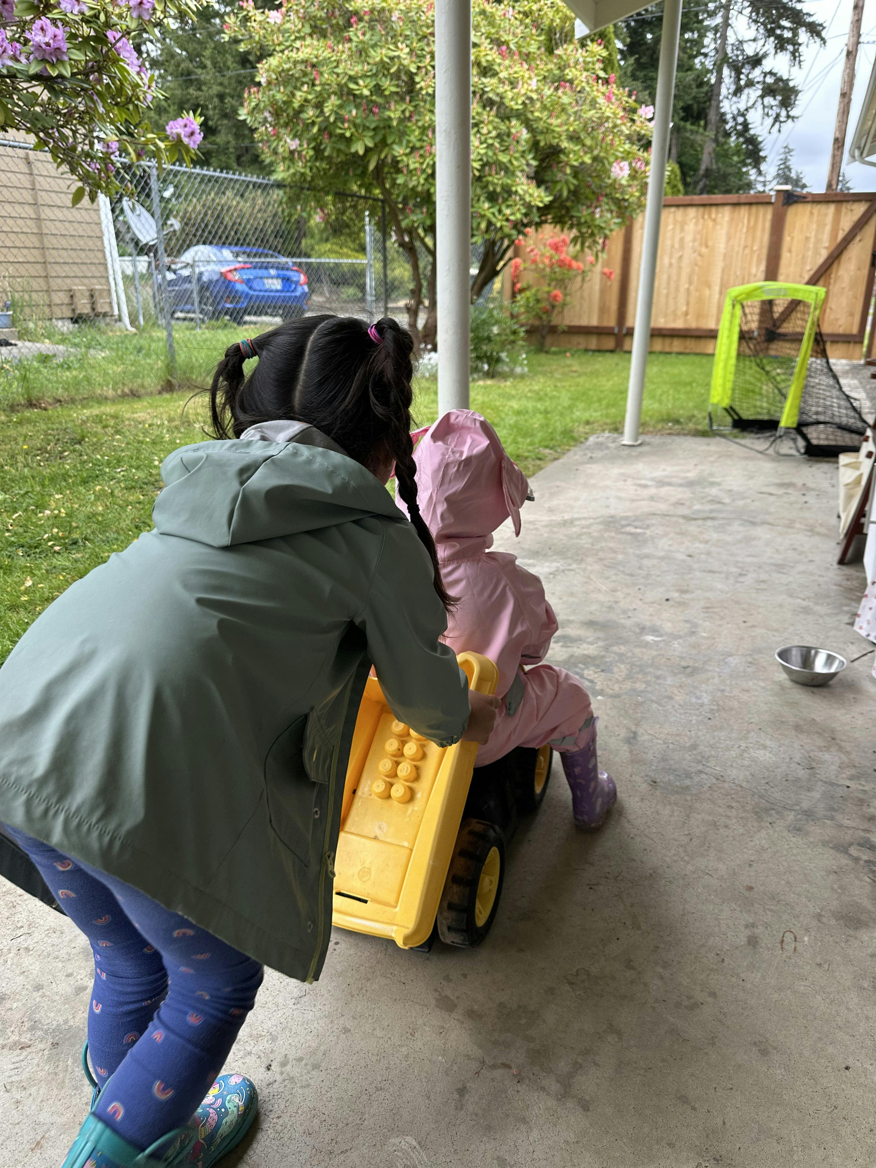 Child pushing another child in a toy vehicle