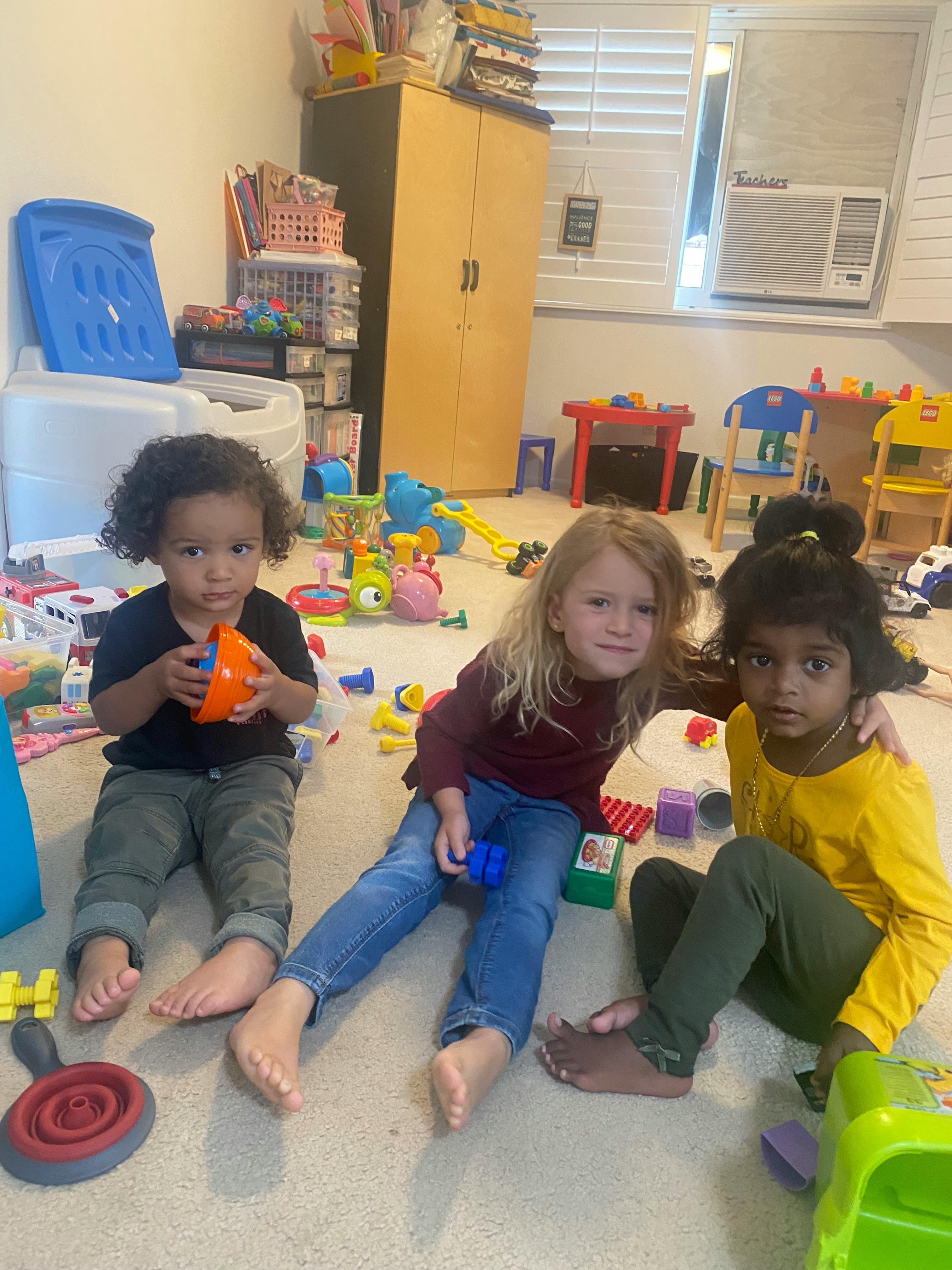 Three children playing with building blocks and toys on a carpeted floor