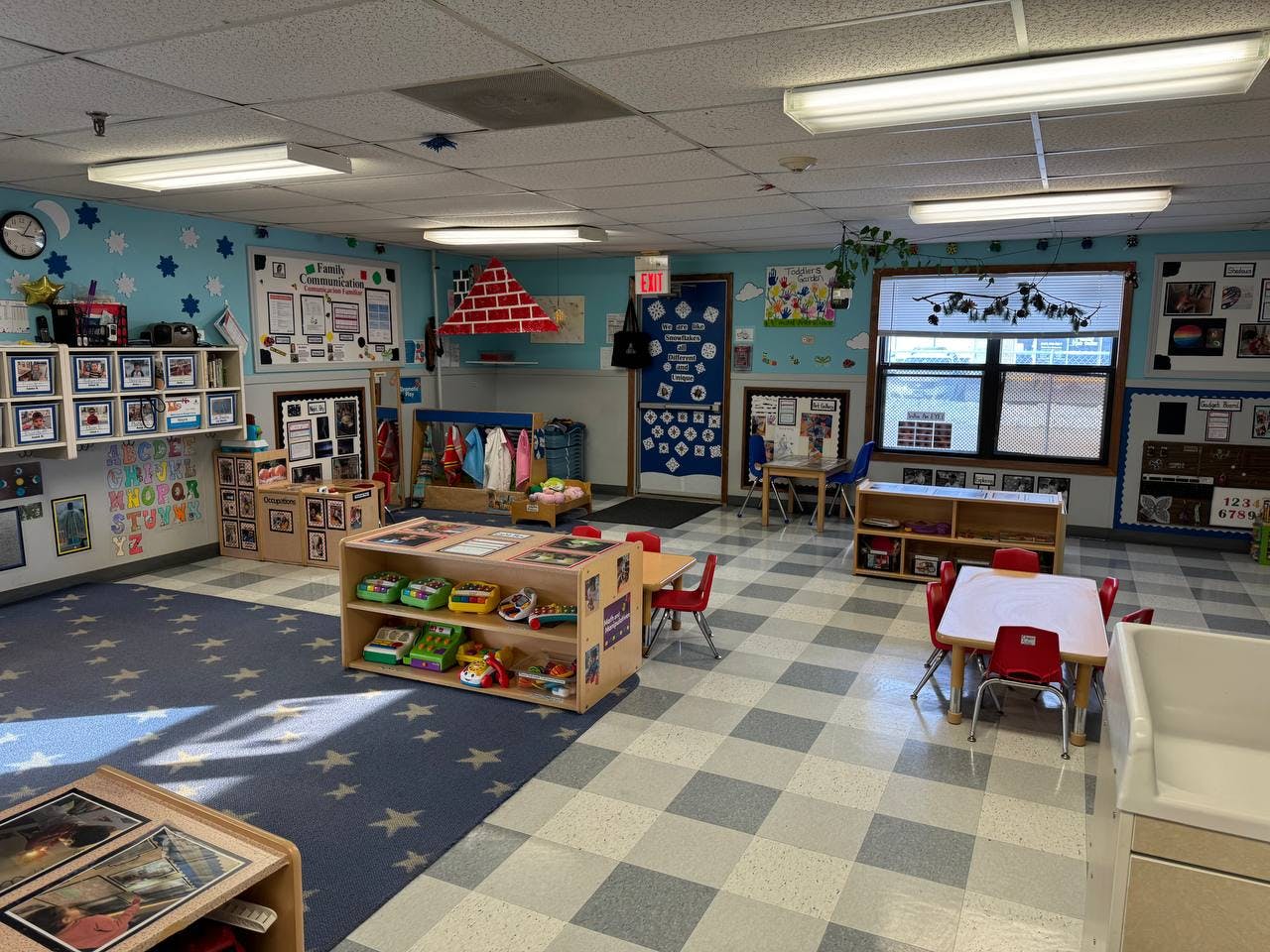 Classroom with child-sized tables, chairs, shelving units with toys, and wall decorations