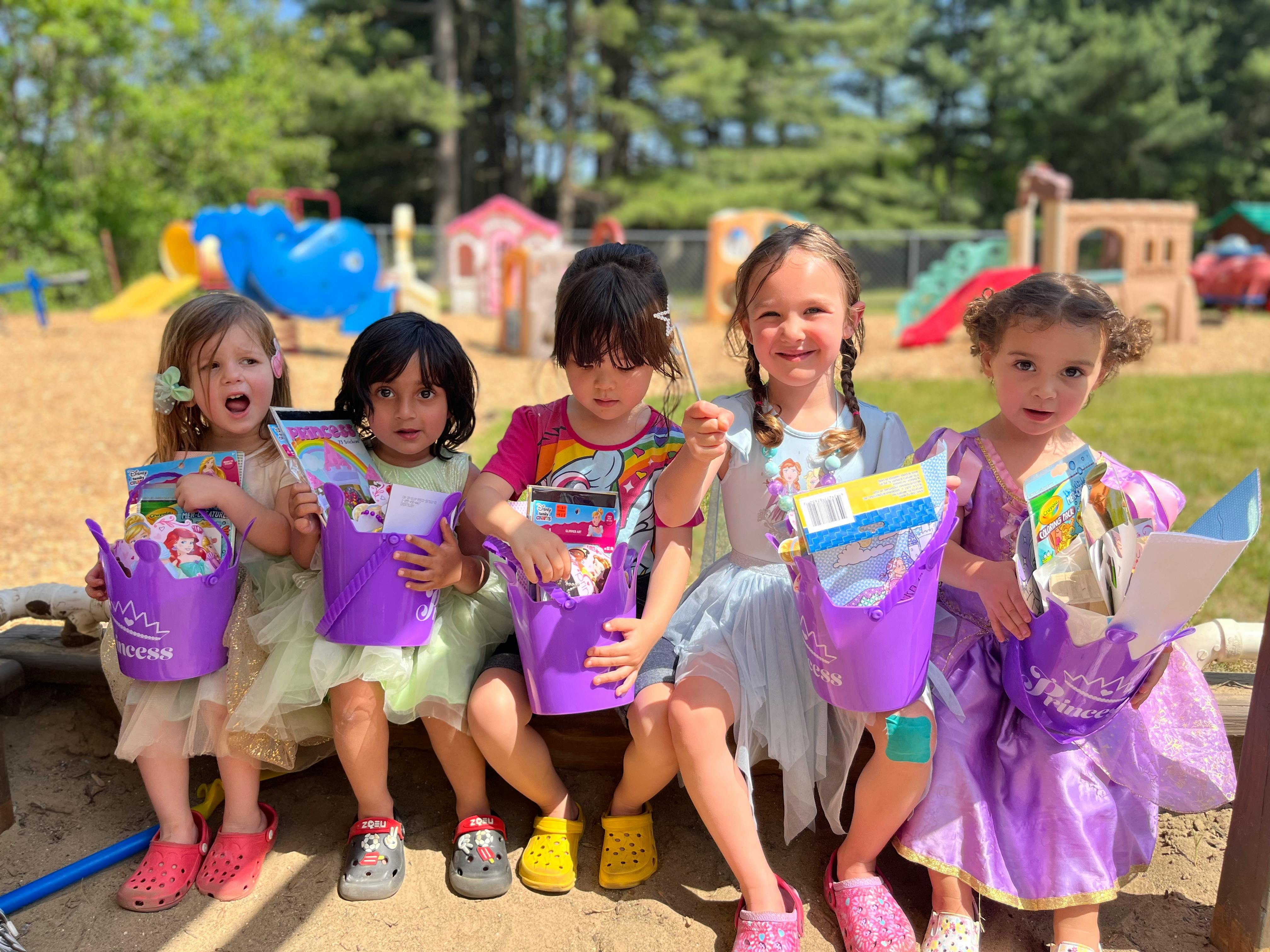 Five children holding purple buckets with items inside, outdoors