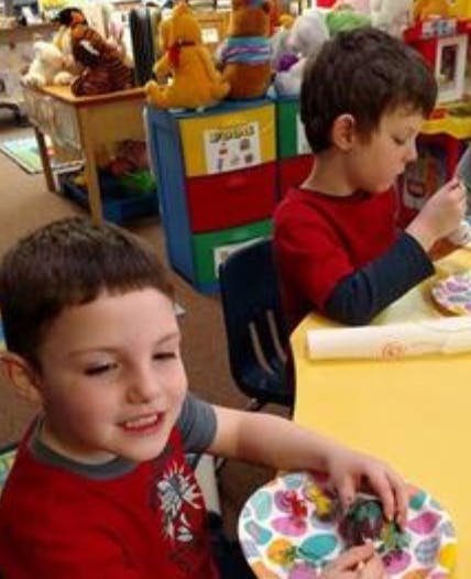 Two children at a table, one looking at the camera, the other focused on an activity