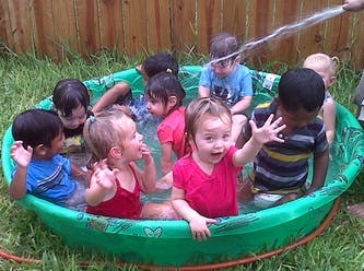Children playing in a small green wading pool with water spraying