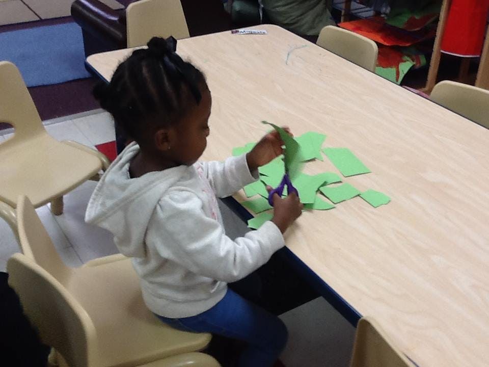 Child cutting green paper with scissors at a table in a classroom
