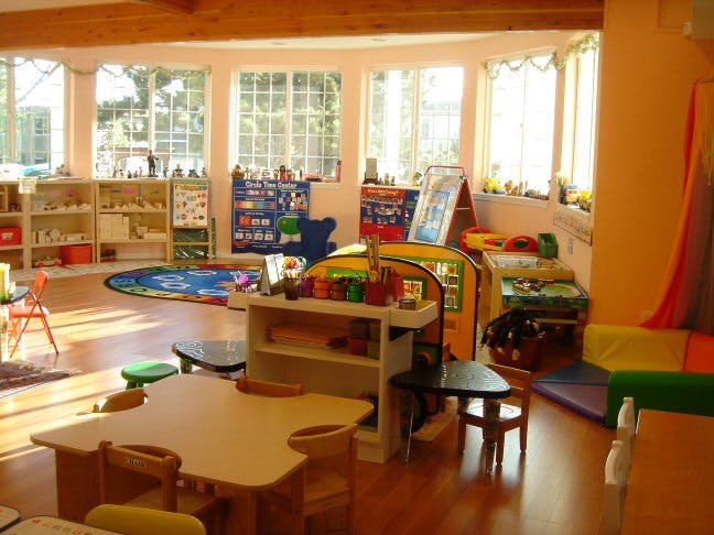 Empty classroom with small tables, chairs, and shelves with toys