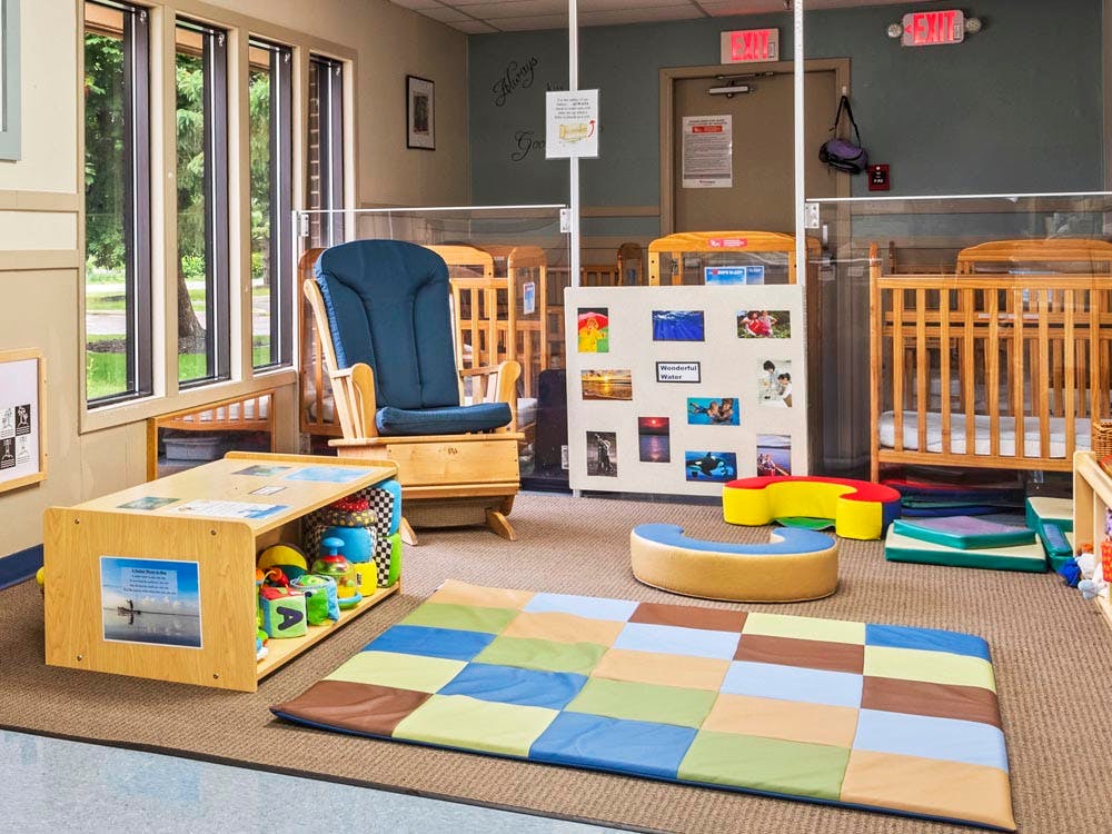 cribs, a rocking chair, and a play mat in a childcare room