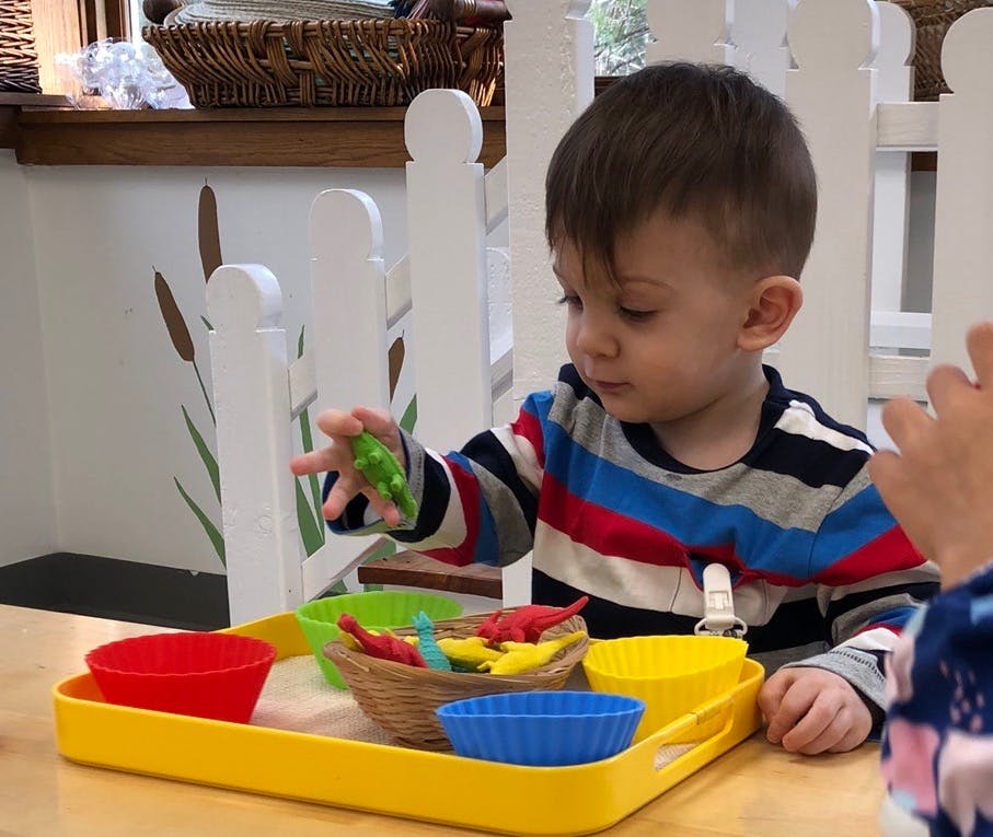 Child playing with small toys in colorful containers on a yellow tray