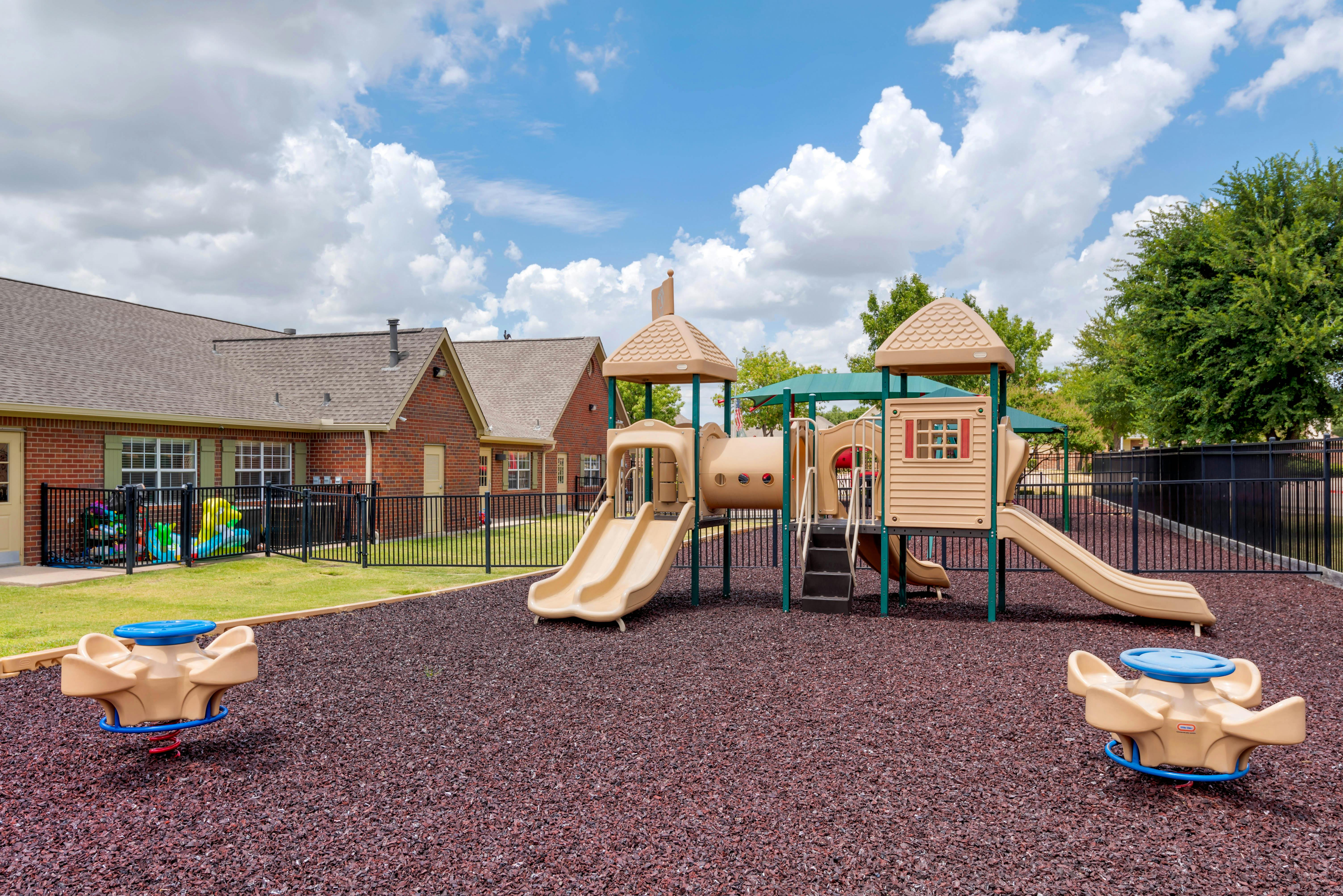 Playground with slides and spring riders on rubber mulch next to a brick building