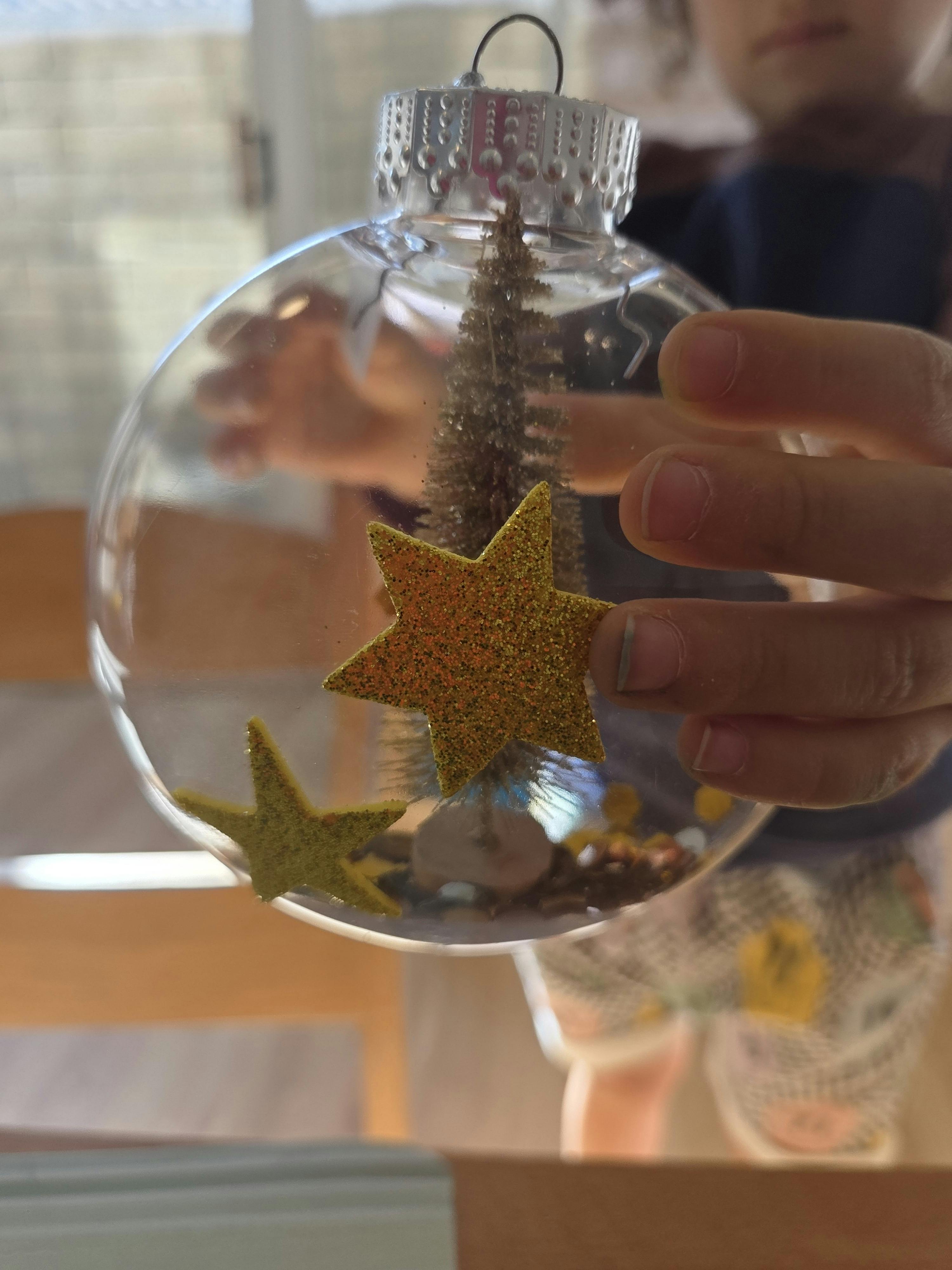 Child holding a clear ornament with a small tree and stars inside