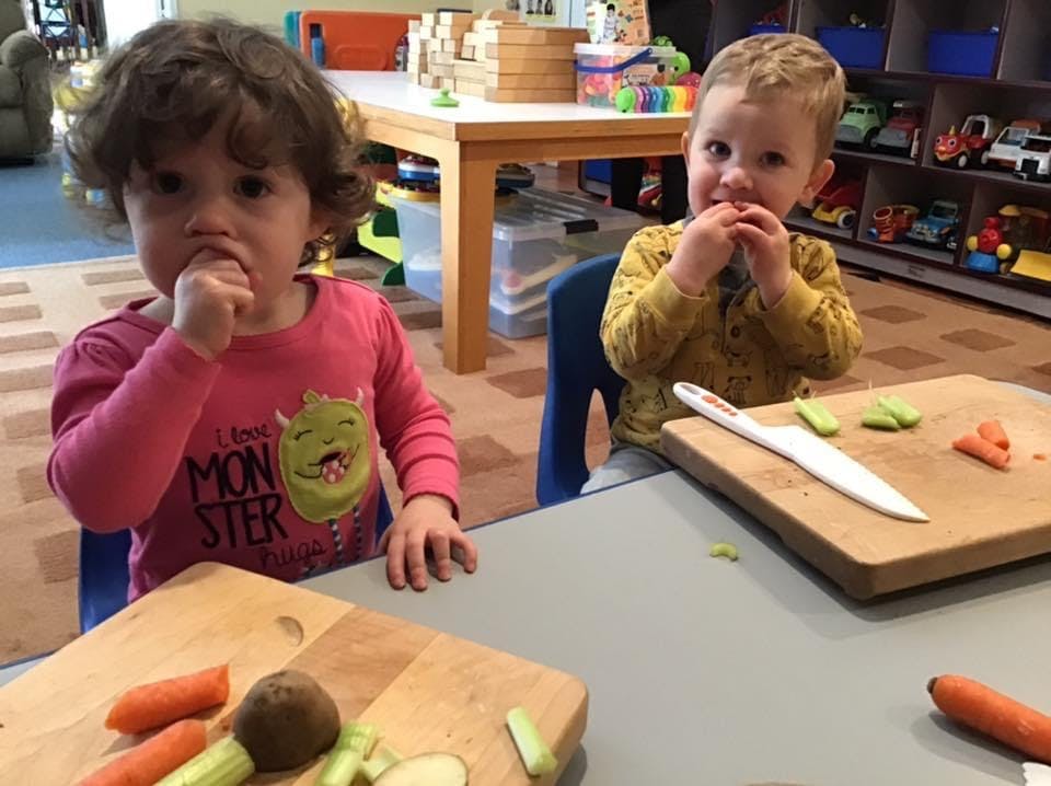 Two children eating food at a table with cutting boards and vegetables