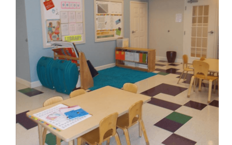 Classroom with child-sized tables and chairs, whiteboards, and a blue rug