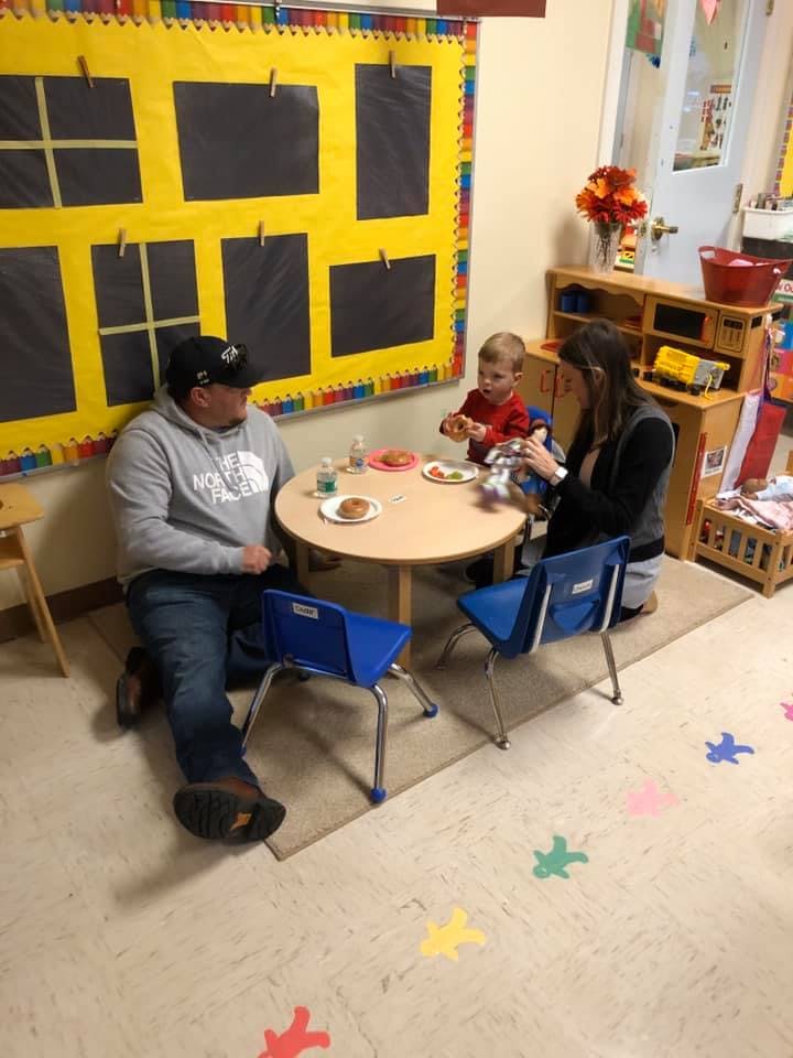 Two adults and a child sitting at a small table in a classroom
