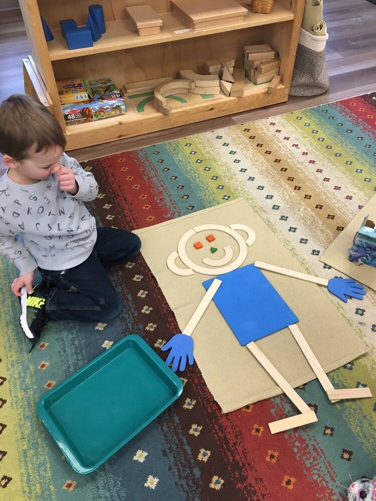 Child on a rug next to a craft project of a person